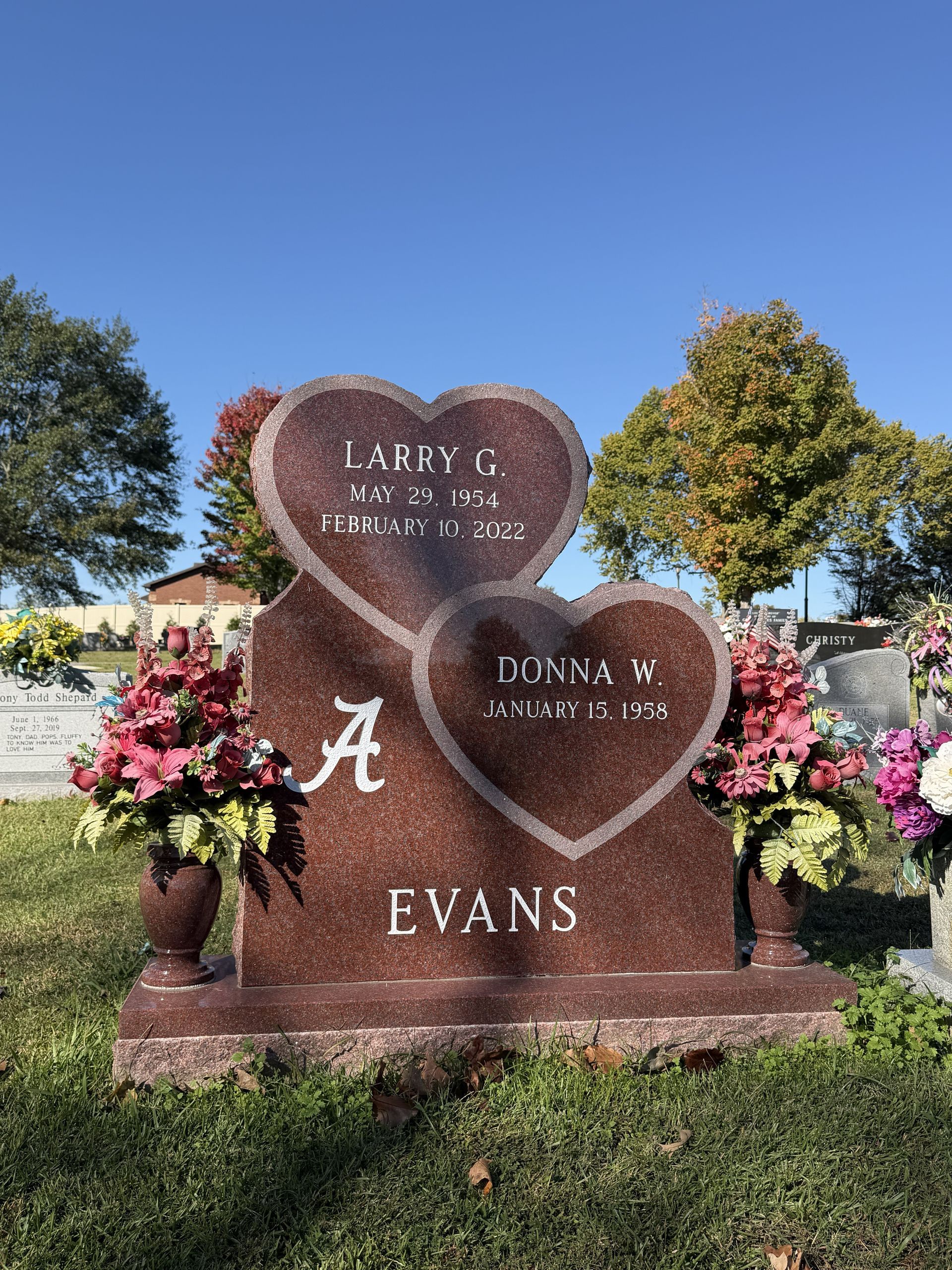 Heart-shaped memorial gravestone with flowers, engraved “EVANS,” in a sunny cemetery.