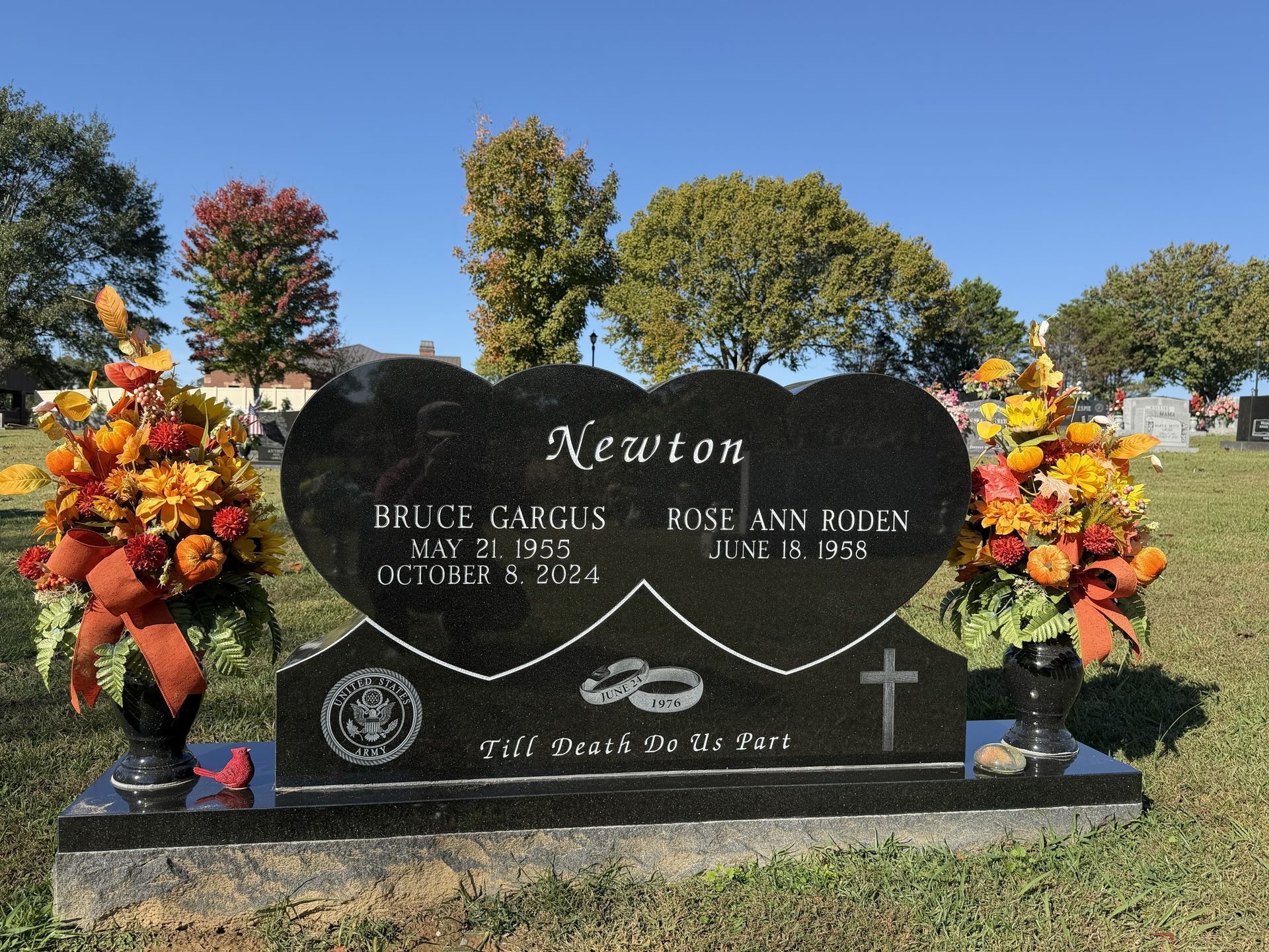 Black granite double gravestone with orange flowers in a cemetery under a blue sky