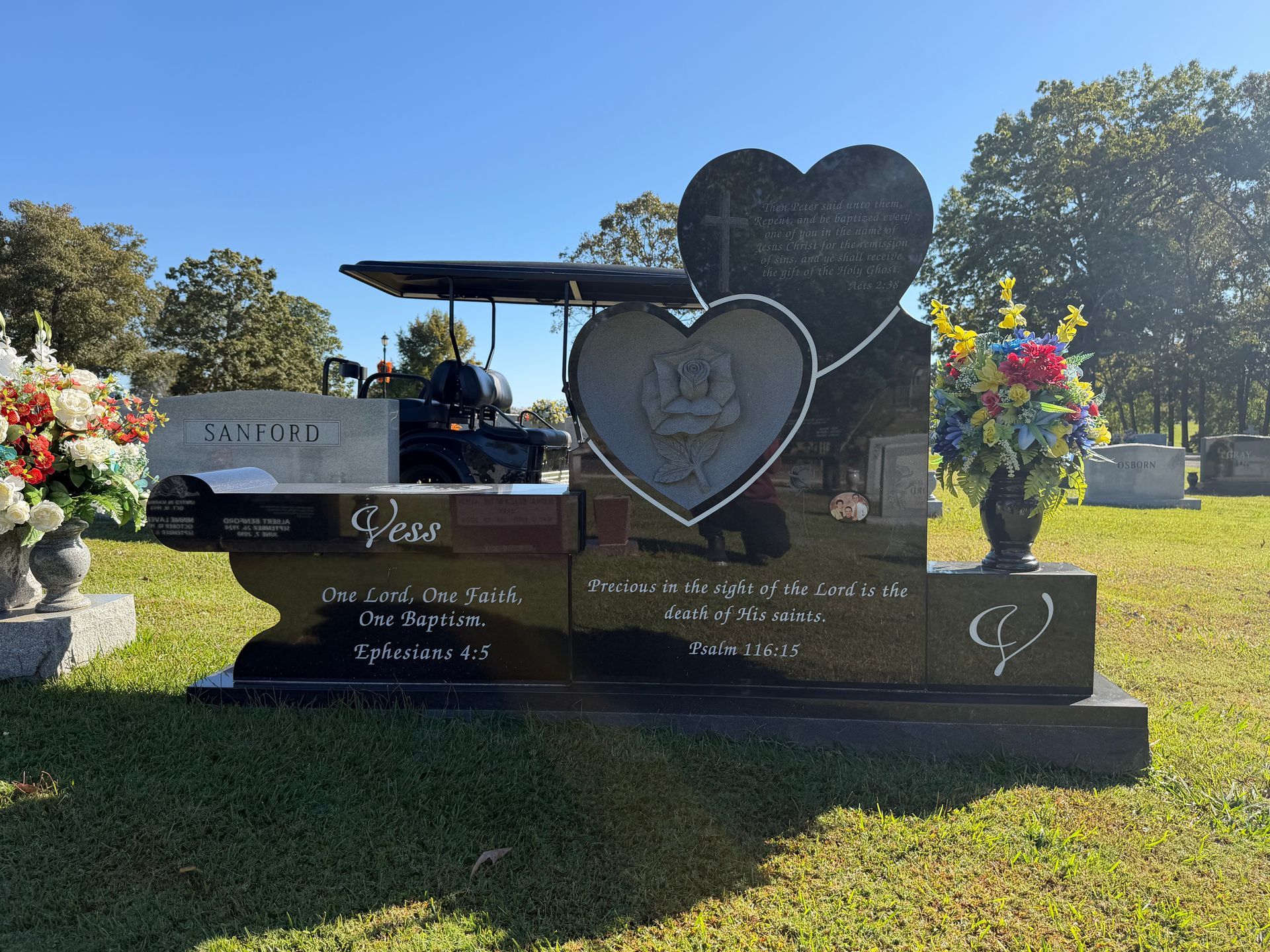 Heart-shaped memorial gravestone with floral tributes in a sunny cemetery