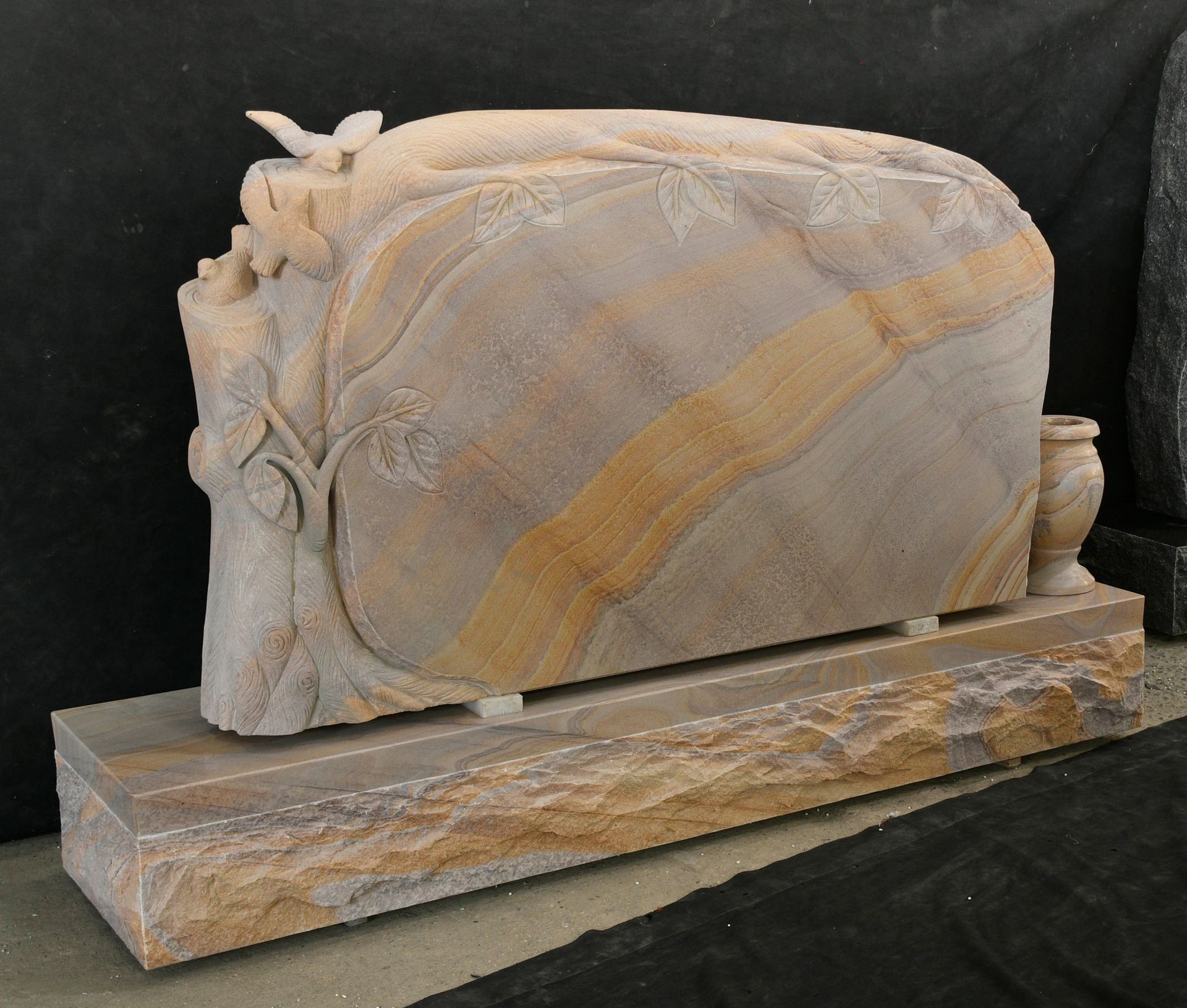Polished stone sculpture with gold veining on a rectangular base against a black background