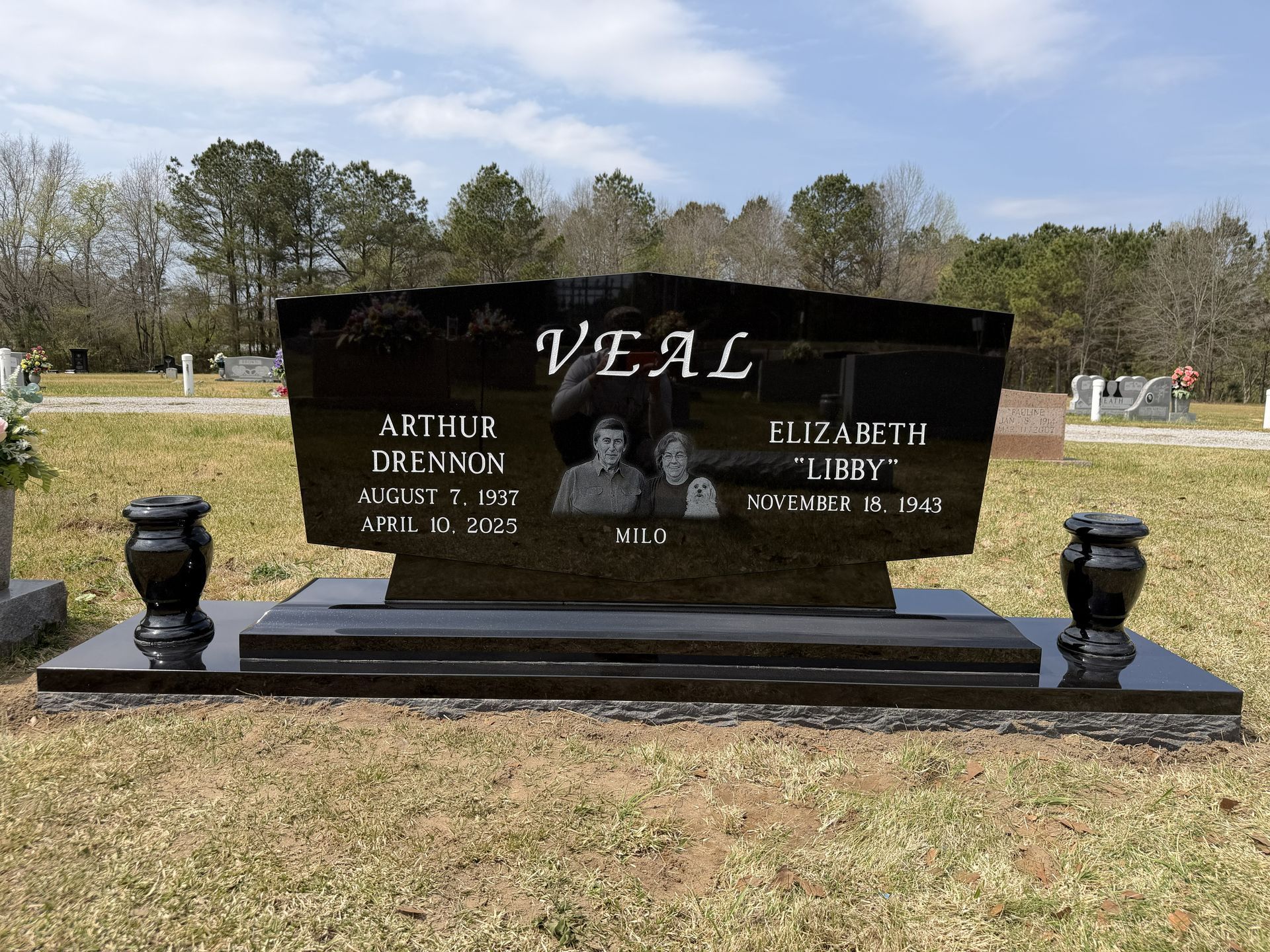Black granite memorial headstone with “VEAL” and two portrait photos in a grassy cemetery.