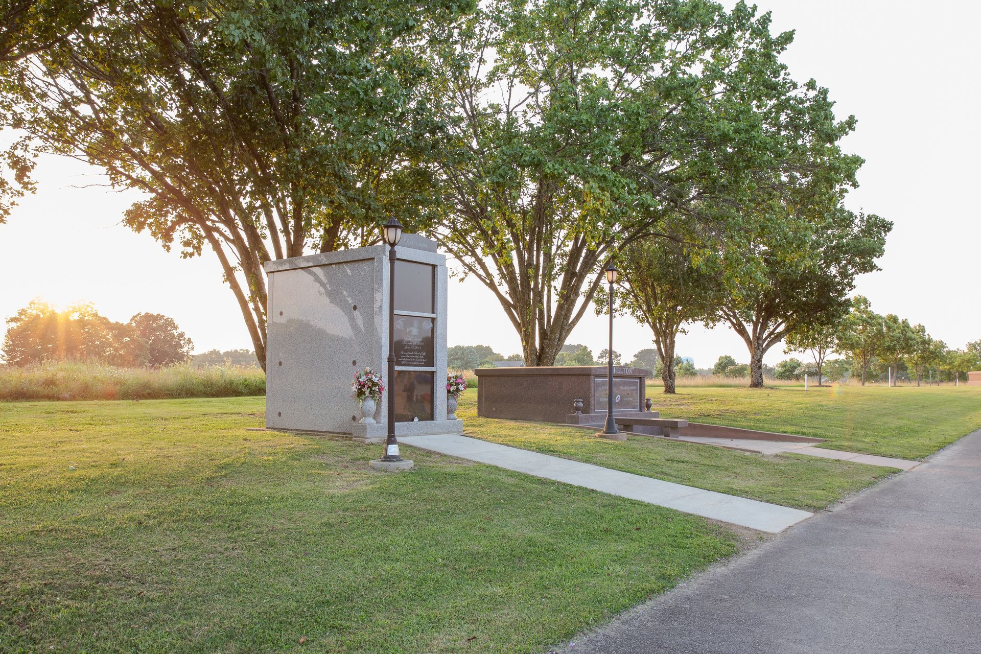 Small concrete memorial plaque in a grassy park with trees and a paved path at sunset