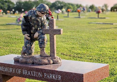 Soldier kneeling at a memorial cross on a gravestone in a cemetery.