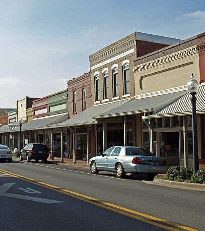 Small-town main street with parked cars and historic storefronts under awnings on a sunny day