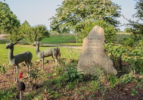 Animal statues in a grassy park beside a stone marker, with trees in the background