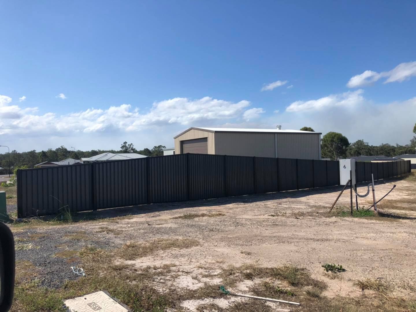 Large Fence Surrounds a Dirt Field With a Building in the Background — Lange's Fencing & Landscaping Centre in Island Plantation, QLD