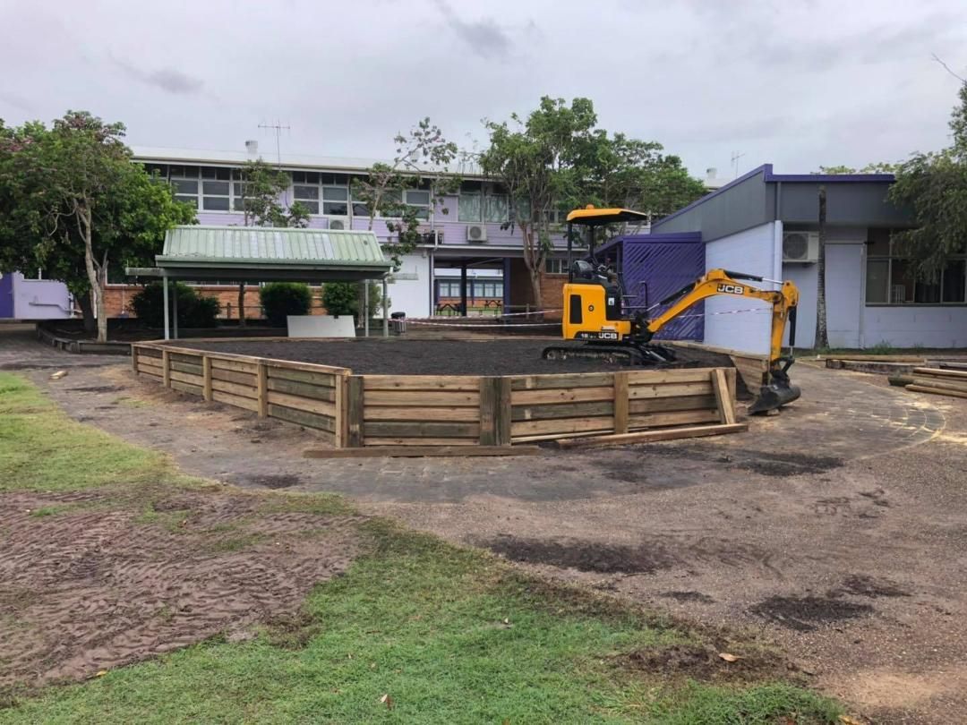 Yellow Excavator is Working on a Wooden Fence in Front of a Building — Lange's Fencing & Landscaping Centre in Island Plantation, QLD