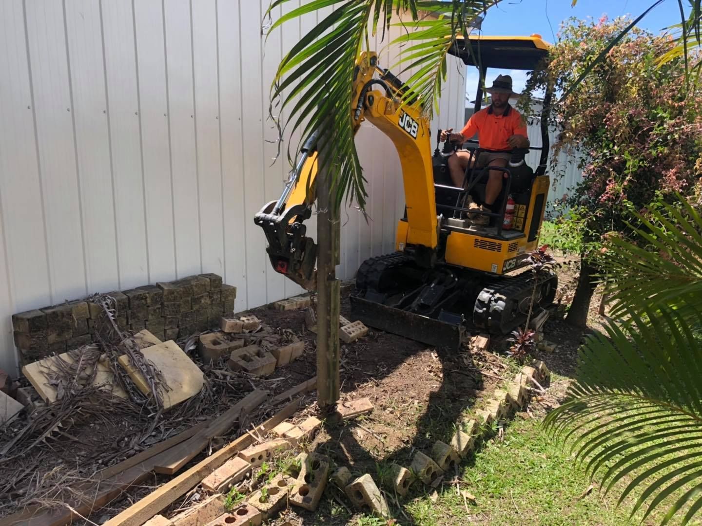 A Man Operating a Yellow Excavator Next to a White Fence — Lange's Fencing & Landscaping Centre in Island Plantation, QLD