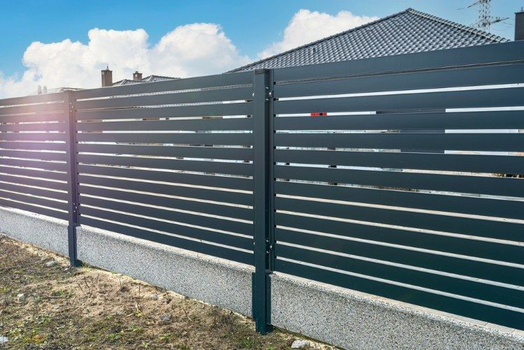 Black Fence is Surrounding a Concrete Wall in Front of a House — Lange's Fencing & Landscaping Centre in Island Plantation, QLD