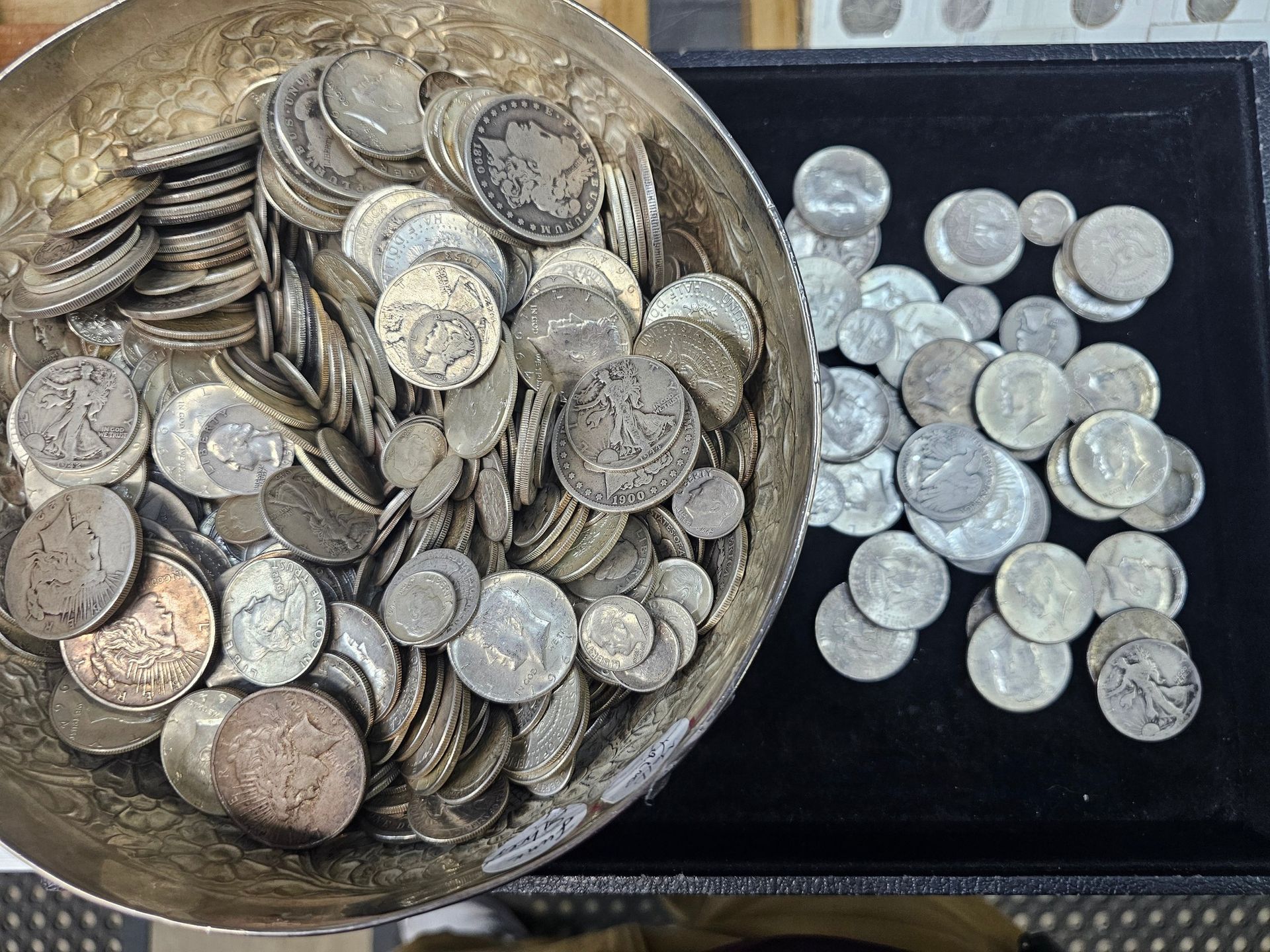 Bowl and tray filled with assorted silver coins on a dark surface
