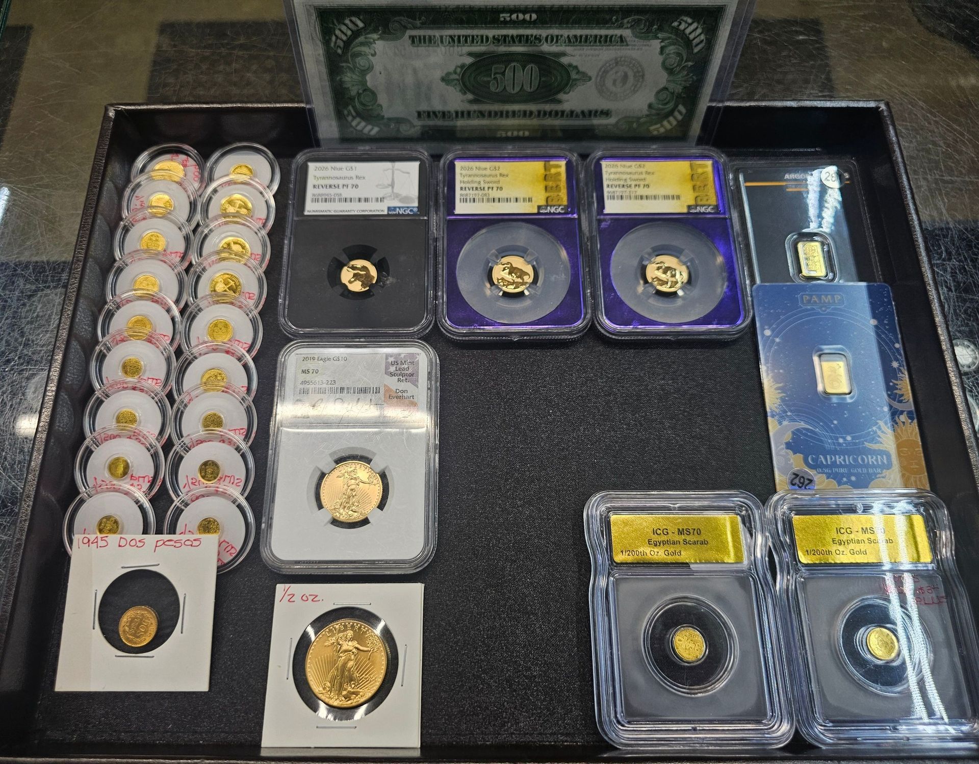 Coin and medal collection in protective cases, arranged on a black tray with one dollar bill at the top.