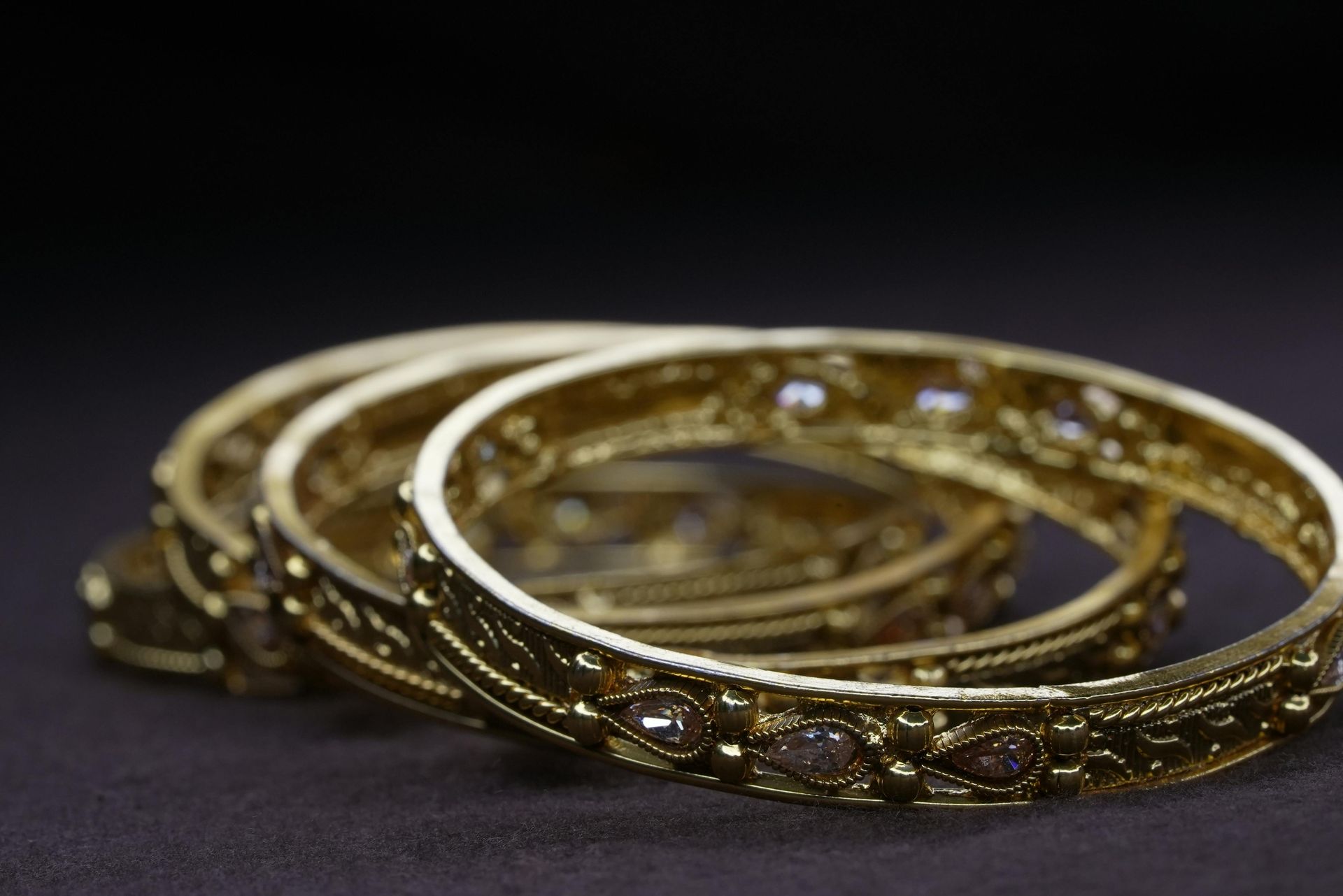 Three ornate gold rings with gemstones stacked on a dark background