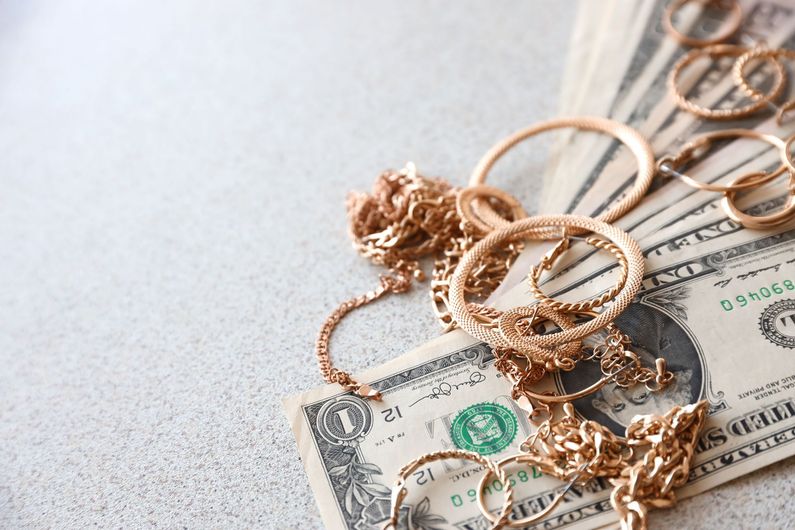 Gold jewelry rings and chains resting on U.S. dollar bills