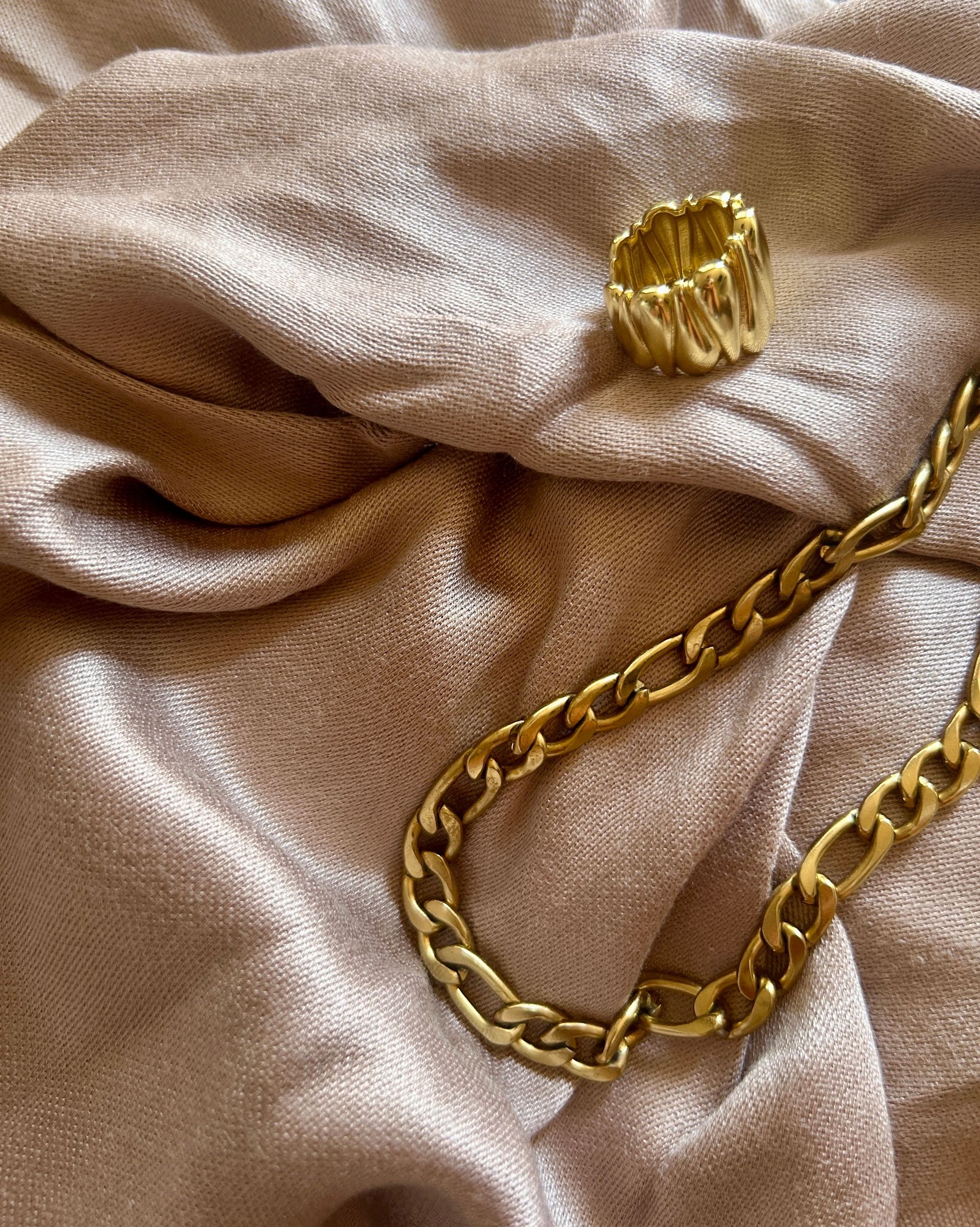 Gold chain and textured gold ring on beige fabric.