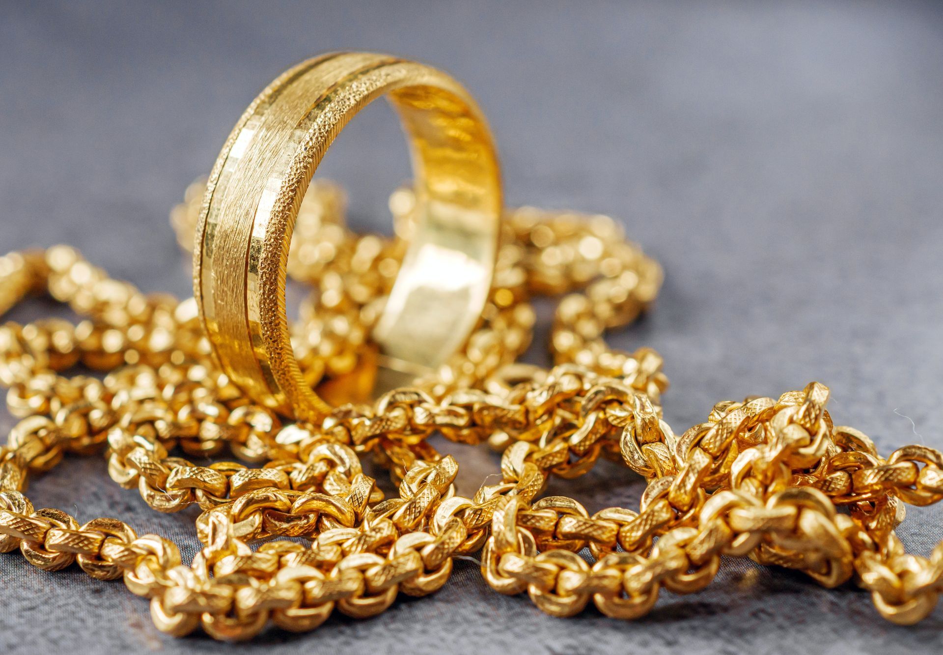 Gold ring resting on a pile of gold chains on a gray surface