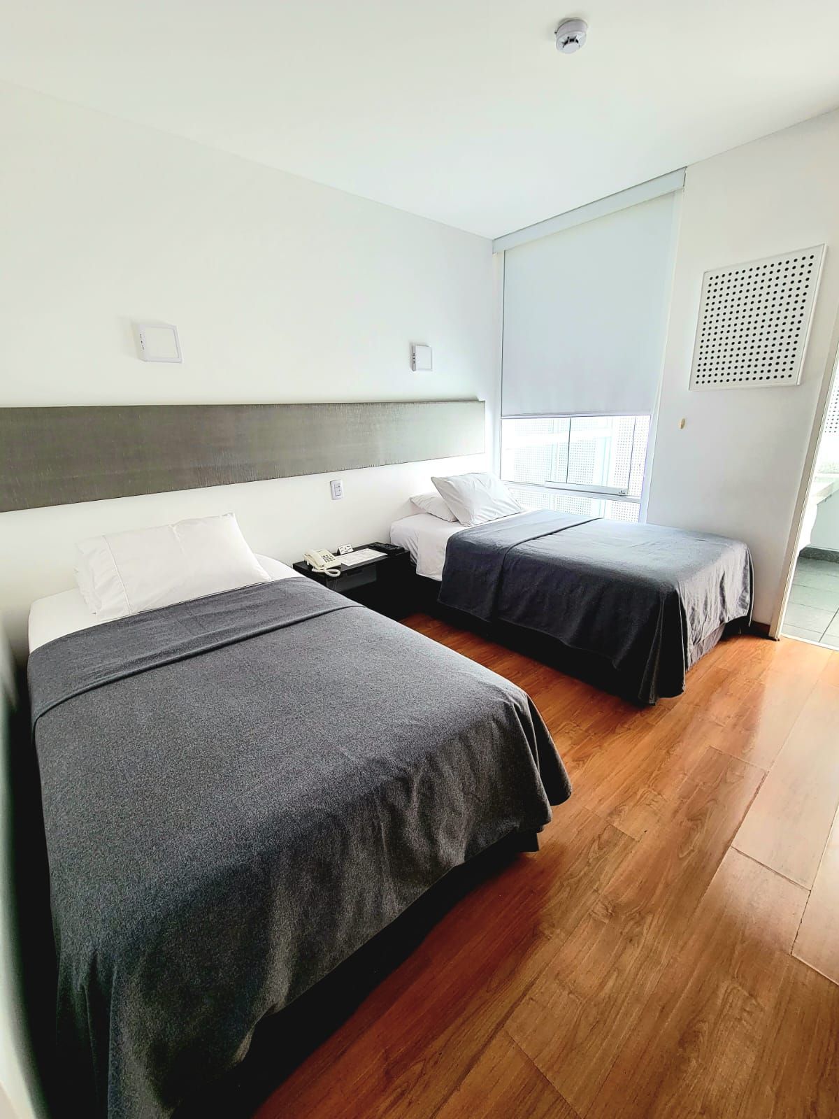 Bright bedroom with two single beds, wood floor, and a window with blinds