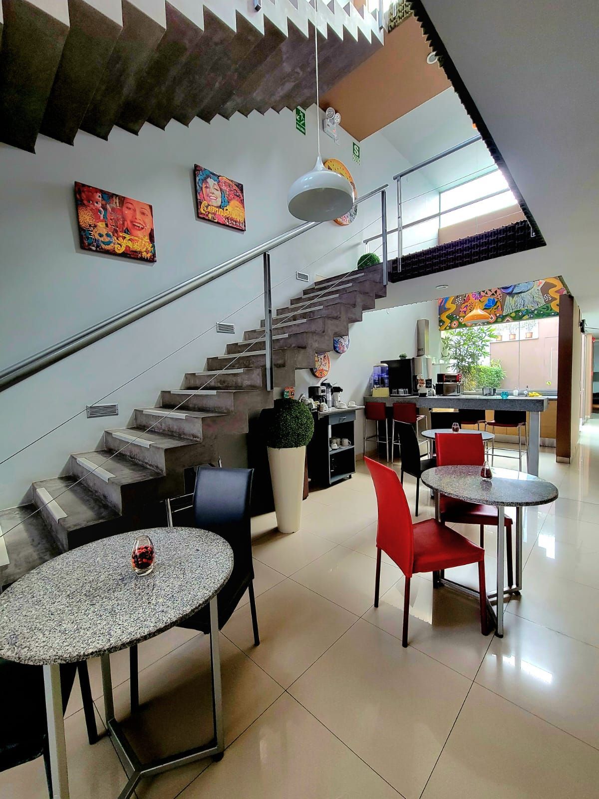 Modern café interior with staircase, red chairs, round tables, and colorful wall art