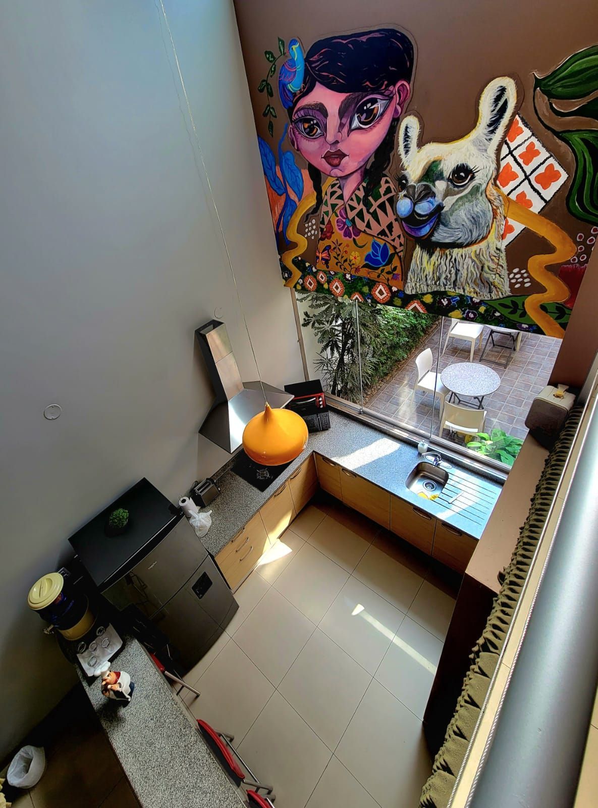 Small balcony nook with a colorful mural, potted plants, and a sink beside a chair and table