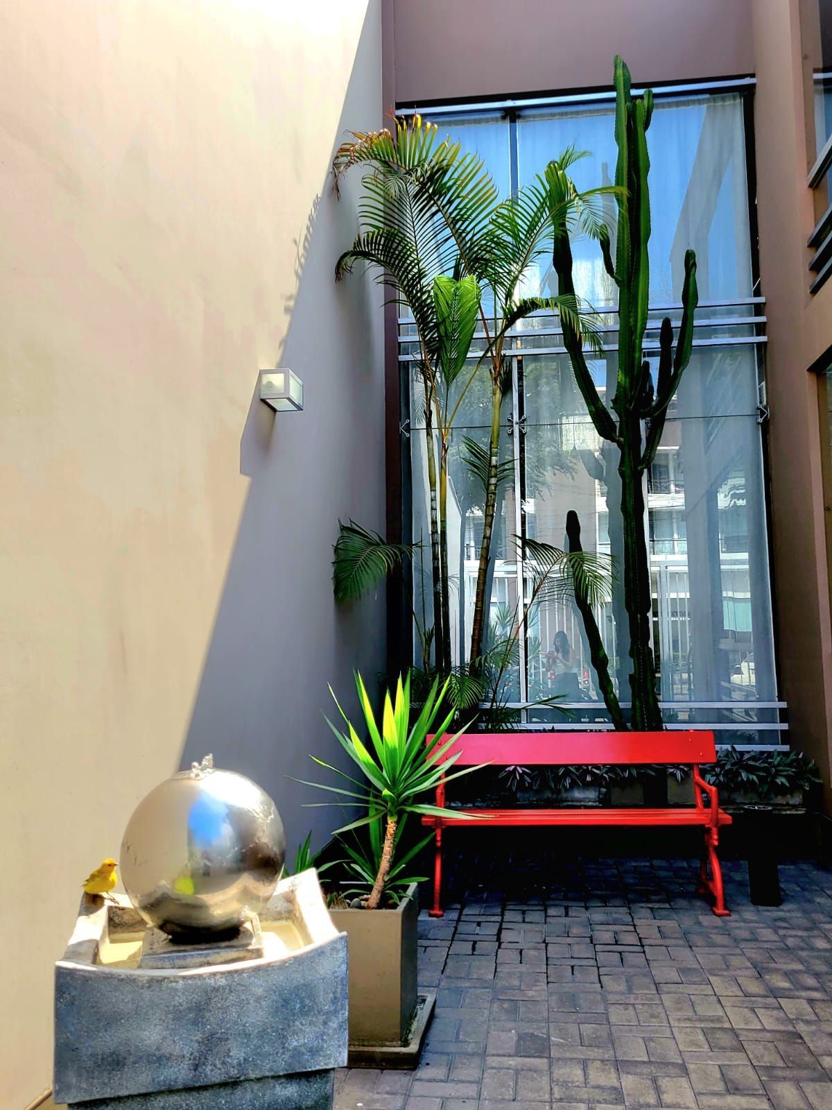 Courtyard with red bench, potted palms, and a reflective silver sculpture by a textured wall