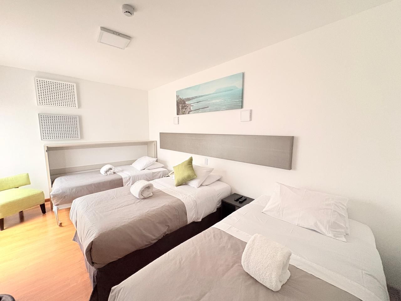 Bright bedroom with three beds, white walls, wood floor, and beach-themed wall art.