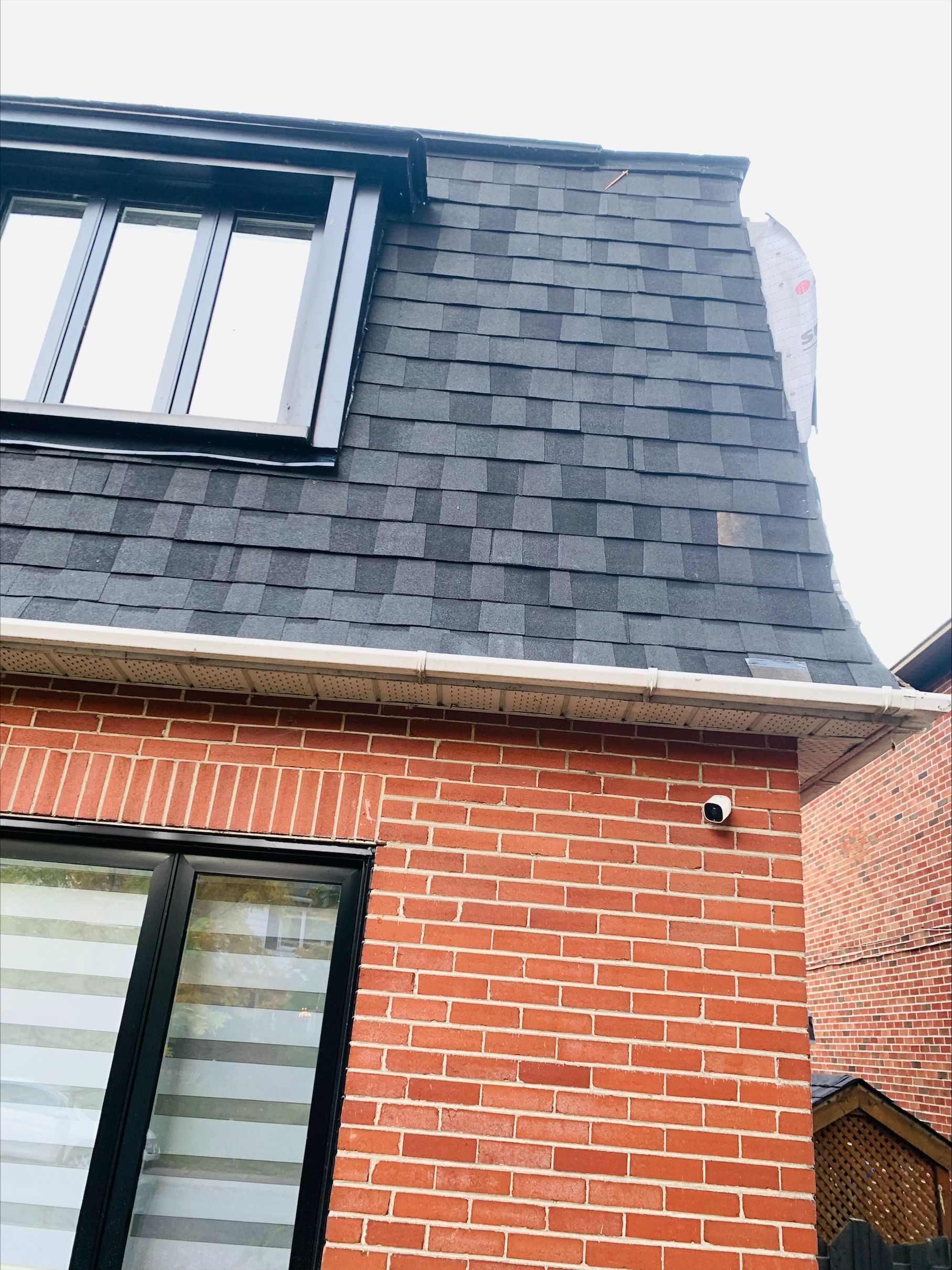 Une maison en brique avec un toit noir et une fenêtre.