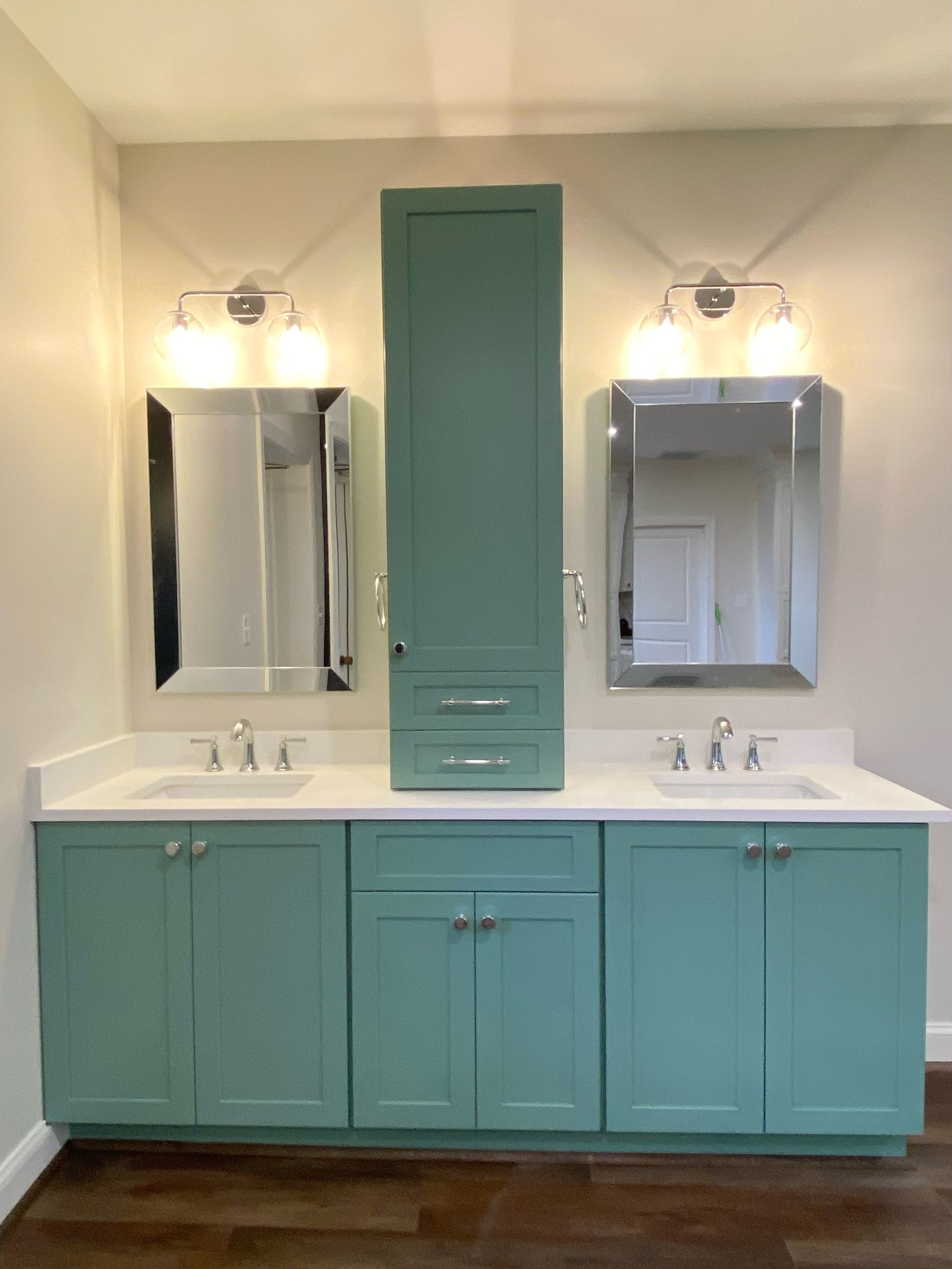 Bathroom with teal cabinets, white countertops, two mirrors, and a tall cabinet.