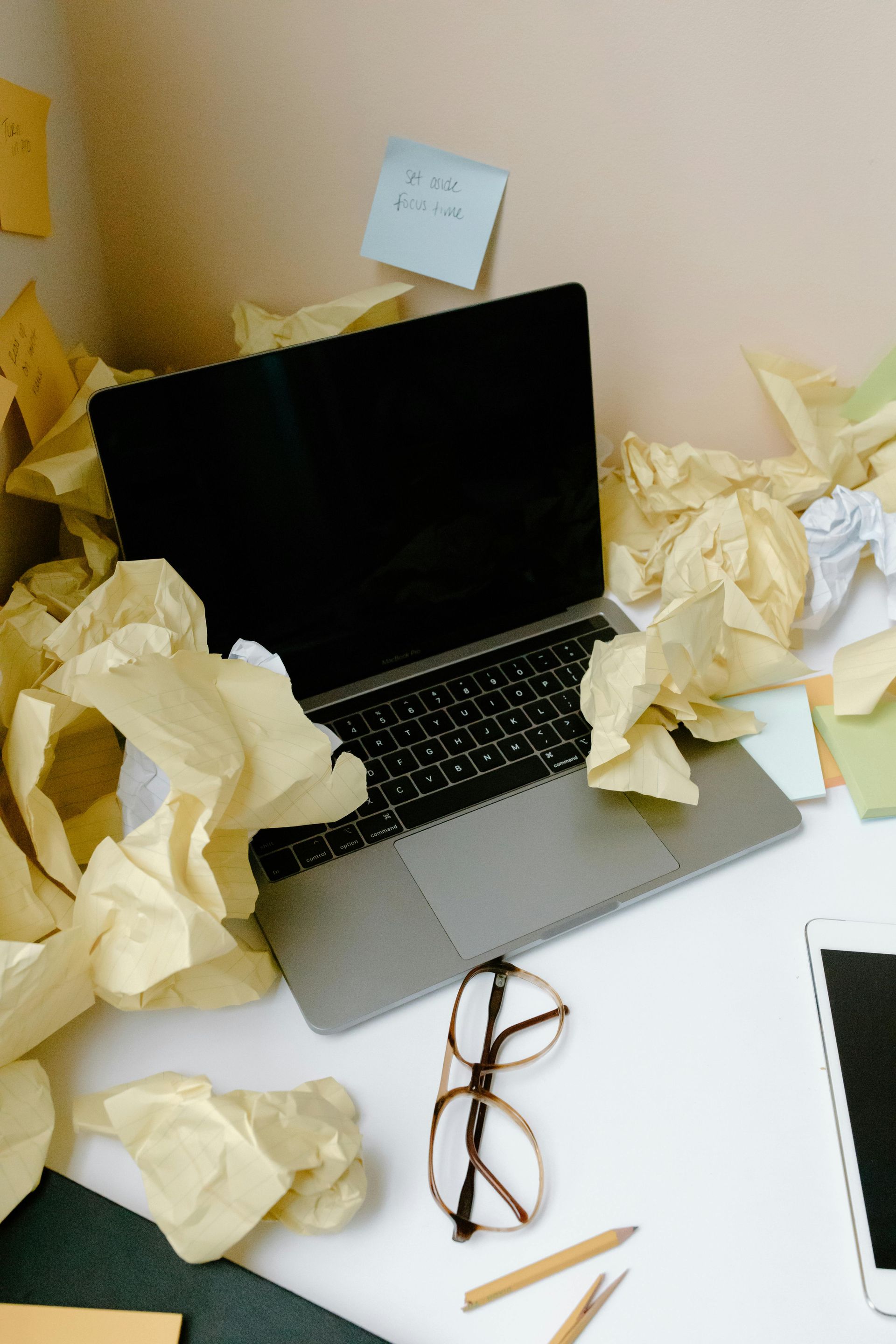 Open laptop on desk surrounded by crumpled paper and office supplies