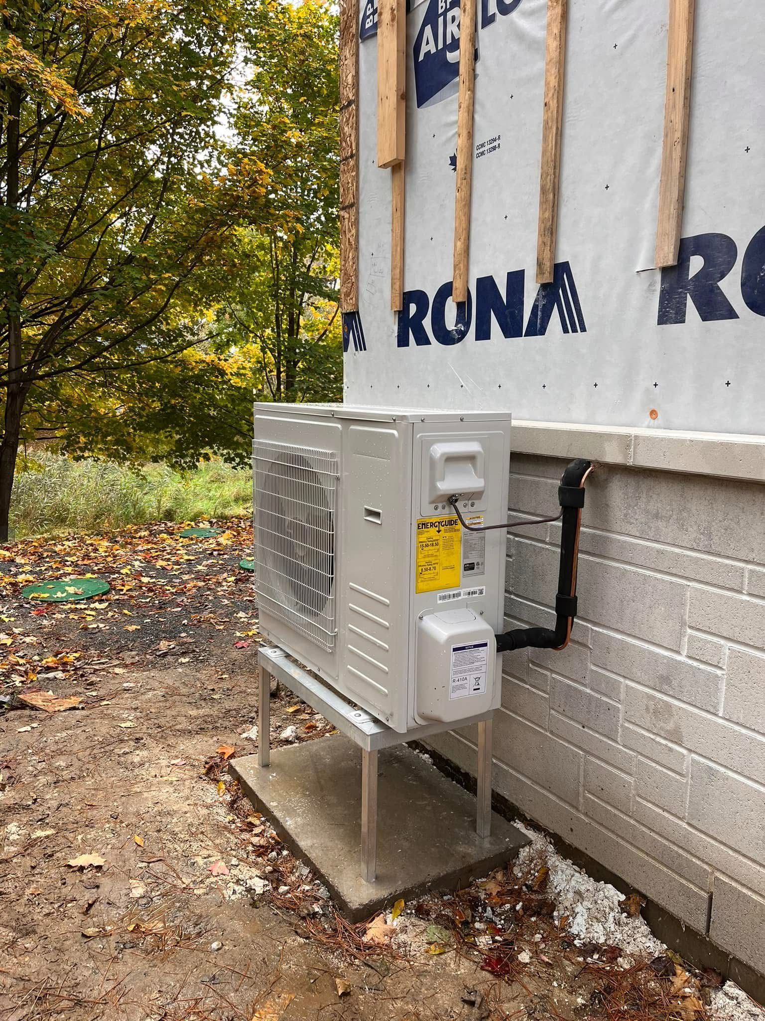 Une unit&eacute; de climatisation install&eacute;e sur un socle en b&eacute;ton contre un mur de brique, adjacent &agrave; un b&acirc;timent en construction av