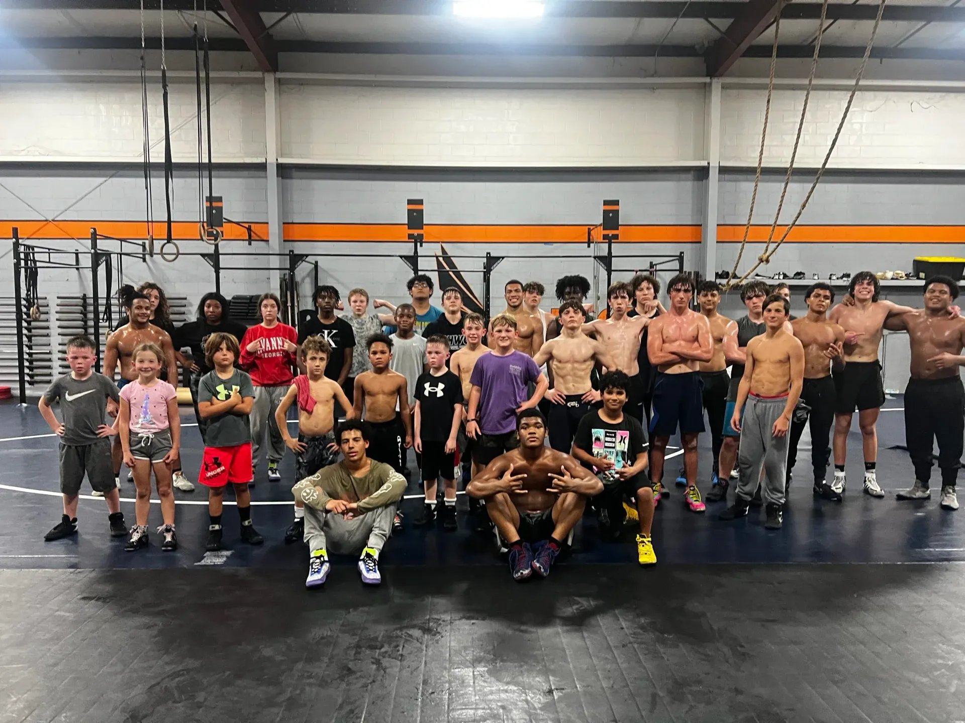 Large group posing in a gym, with several people raising their fists in front of hanging rings and pull-up bars.