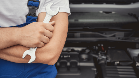 A mechanic holding a wrench in front of a vehicle 