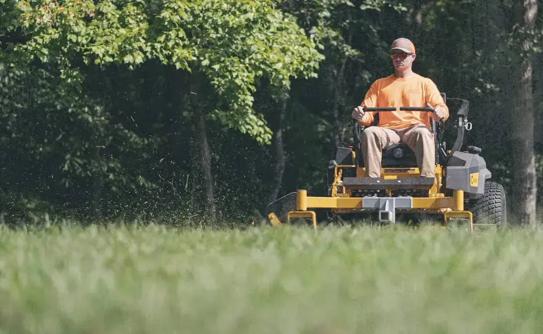 Man mowing a large, lush green lawn on a bright sunny day with a professional yellow ride-on lawn mower
