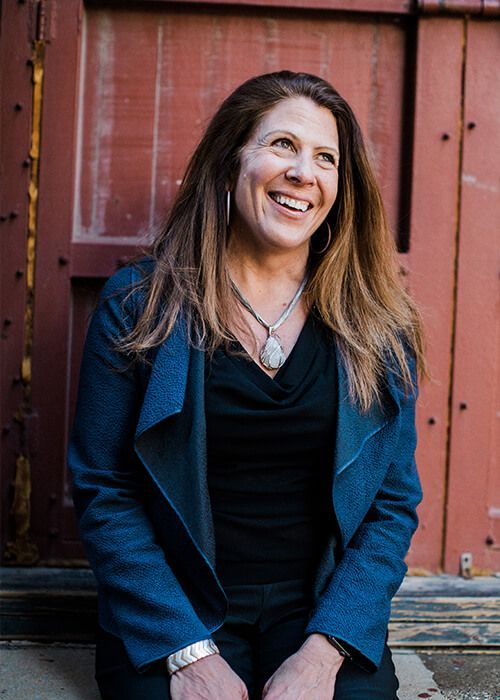 A woman is sitting in front of a red door and smiling.