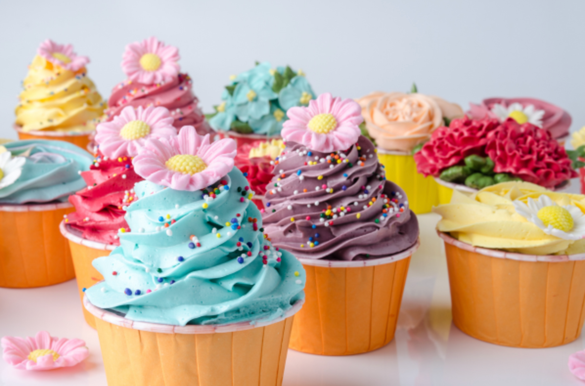 A bunch of colorful cupcakes with frosting and flowers on top.
