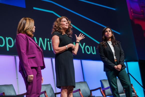 Three women are standing on a stage giving a presentation.