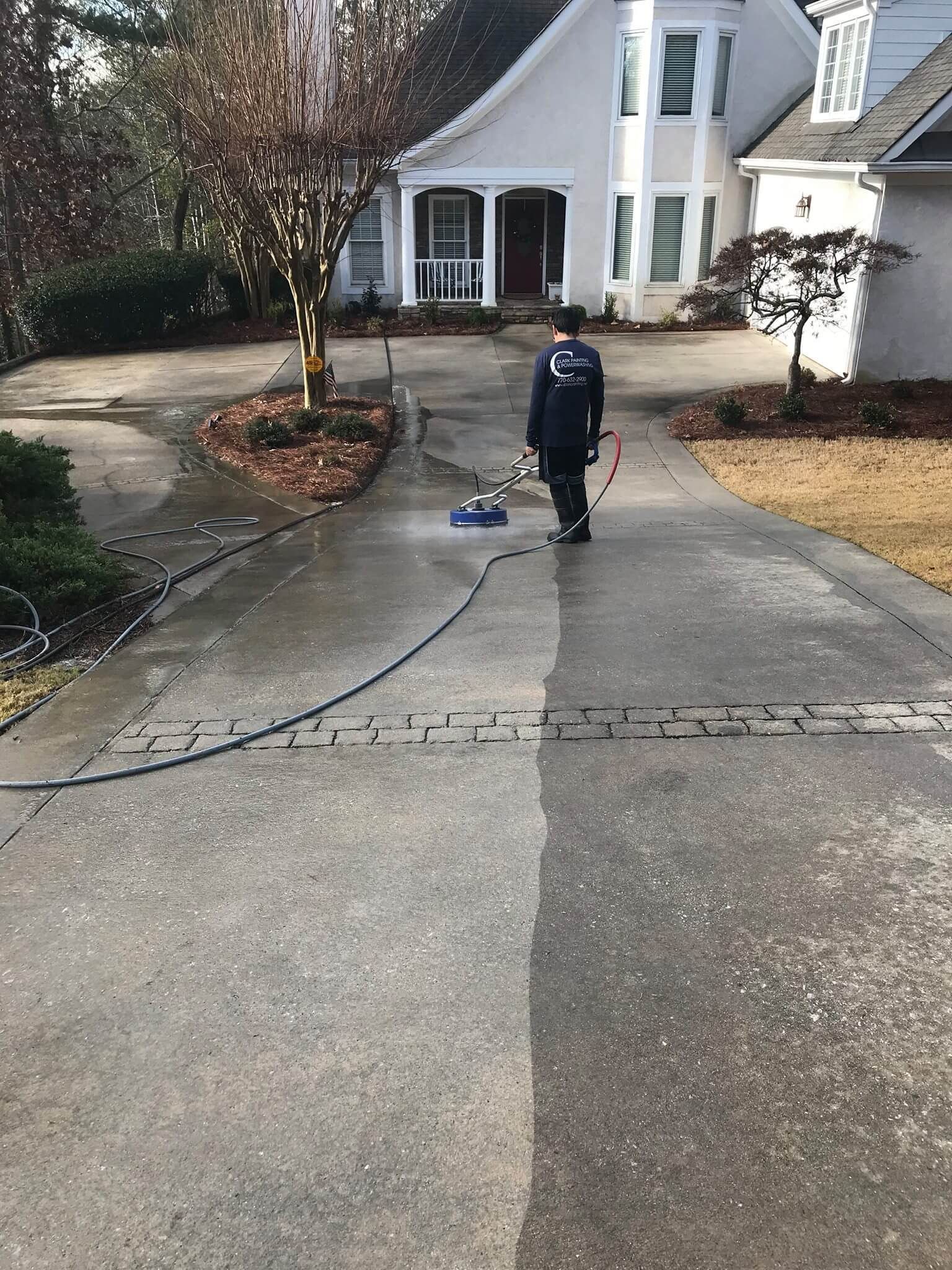 A man is cleaning a driveway in front of a house.