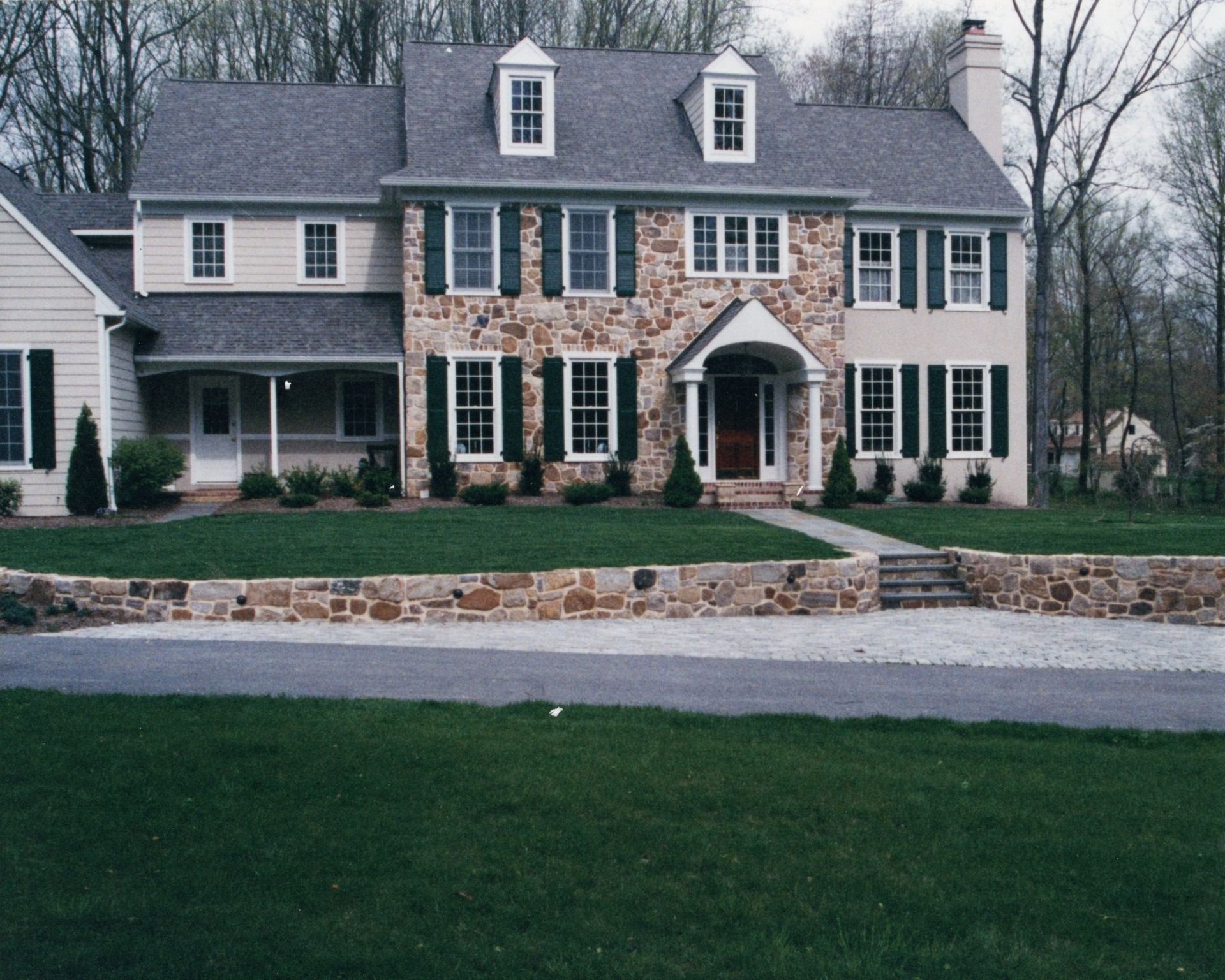 Modern two-story suburban house with stone exterior, front yard, and a driveway at sunset