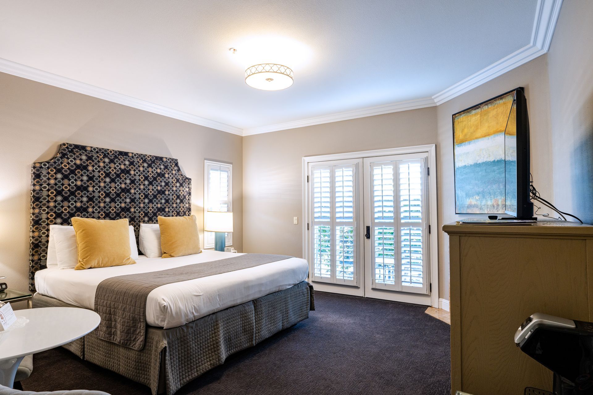 Bedroom with king-sized bed, patterned headboard, and shuttered doors.  Neutral colors and artwork.