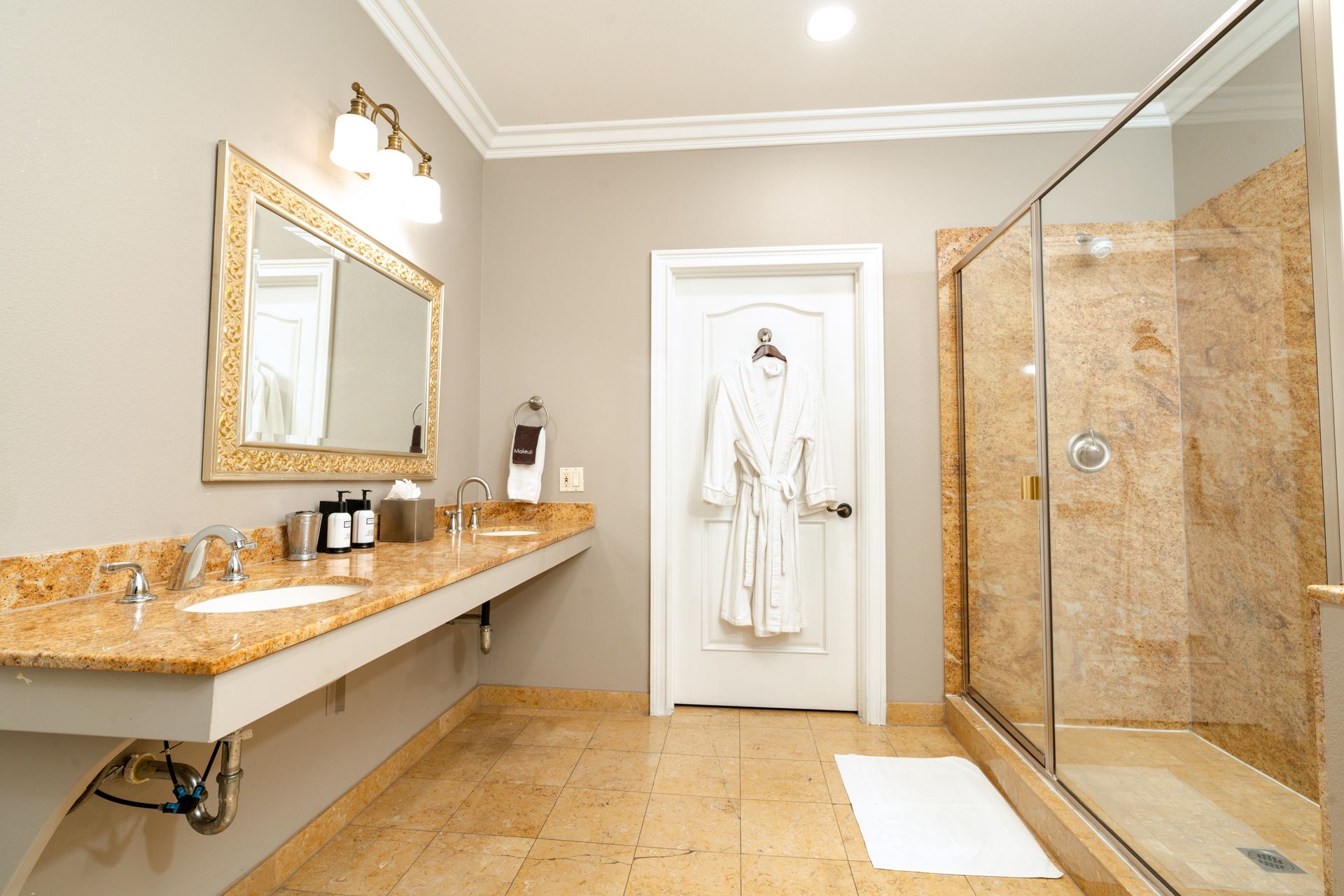 Bathroom with granite countertops, large mirror, and glass shower. Robe hangs on the door.