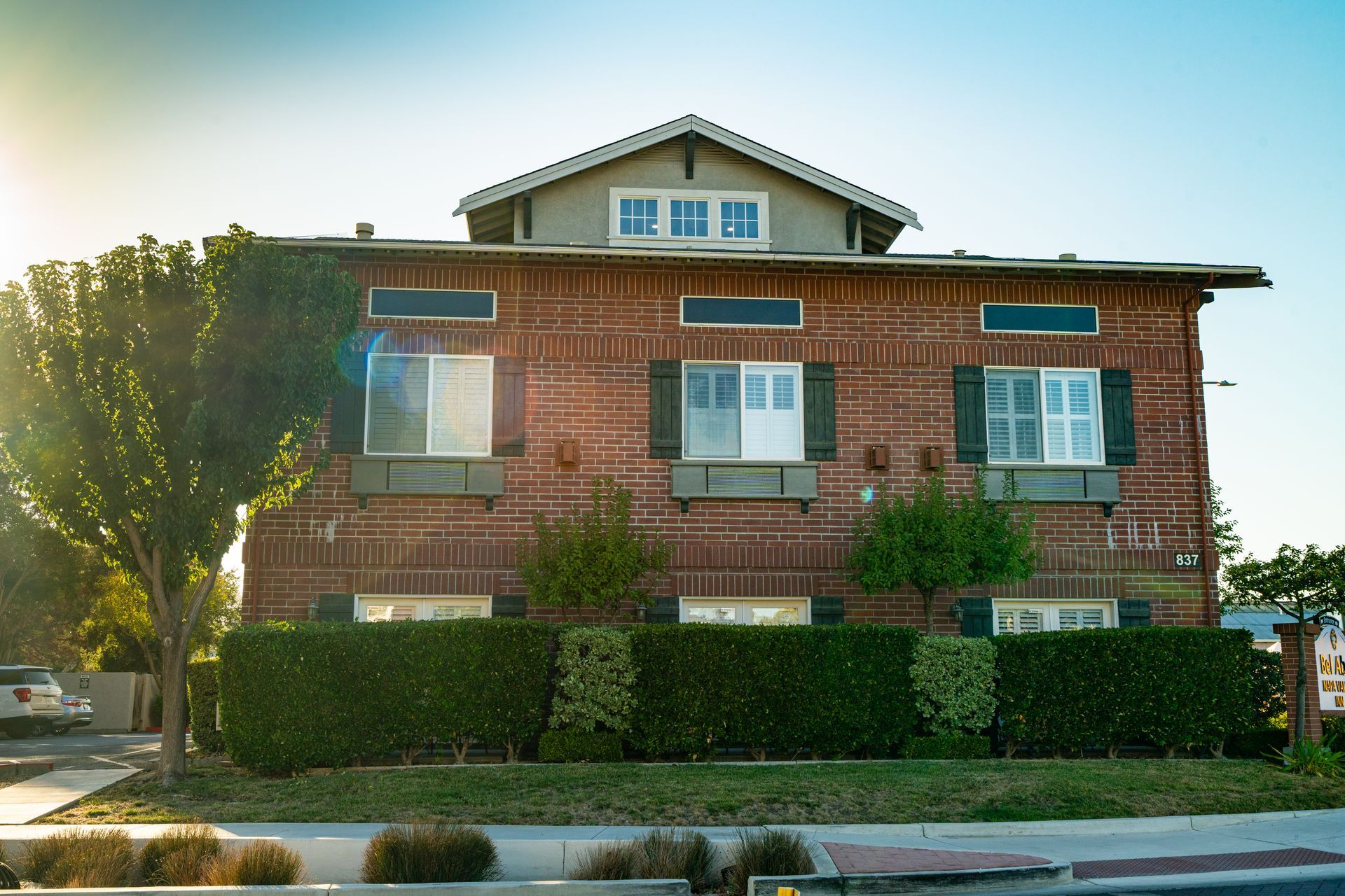 Two-story brick building with green shrubs and trees in front.