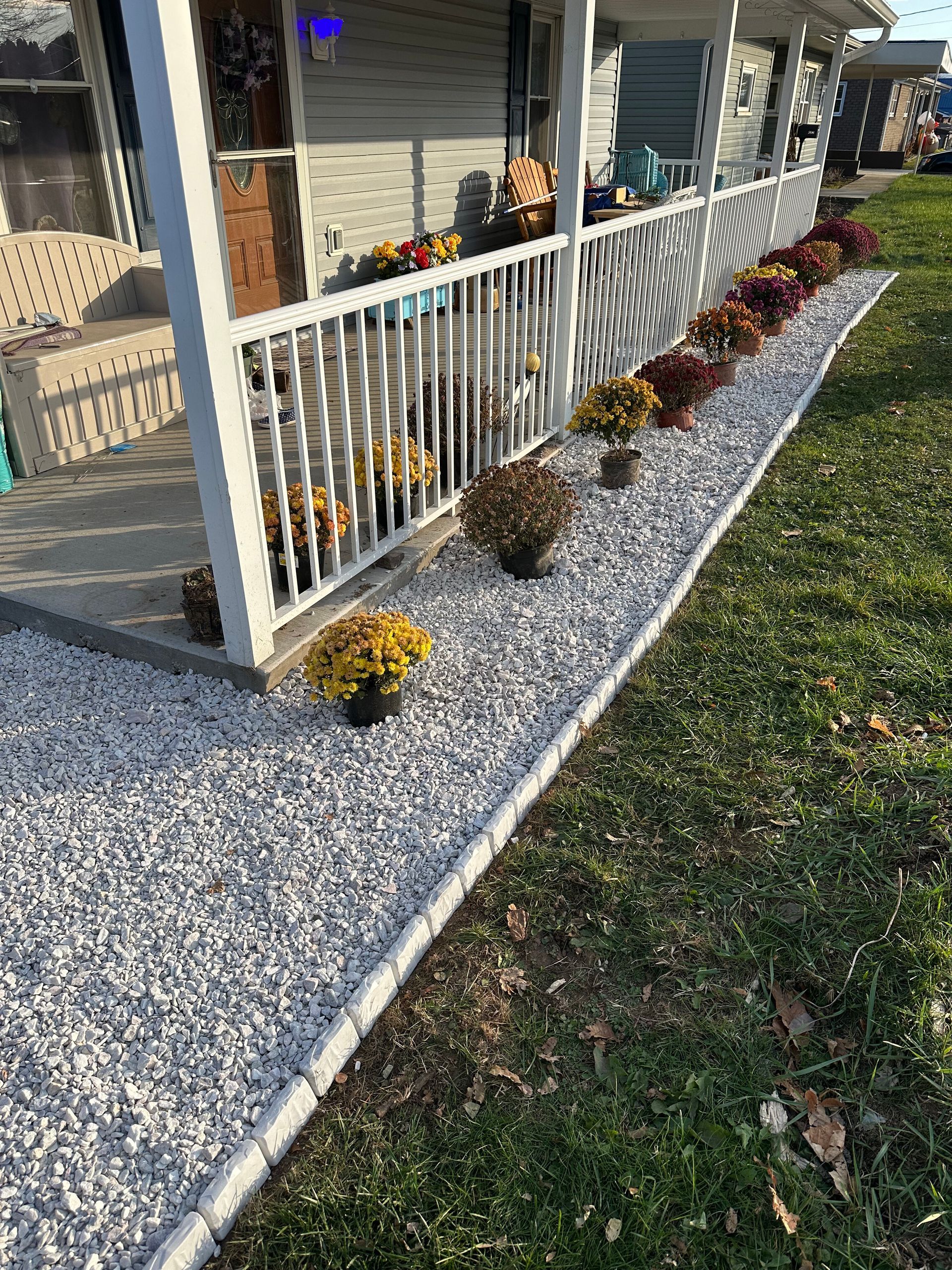 White porch railing with potted flowers beside a gravel walkway and lawn on a sunny day