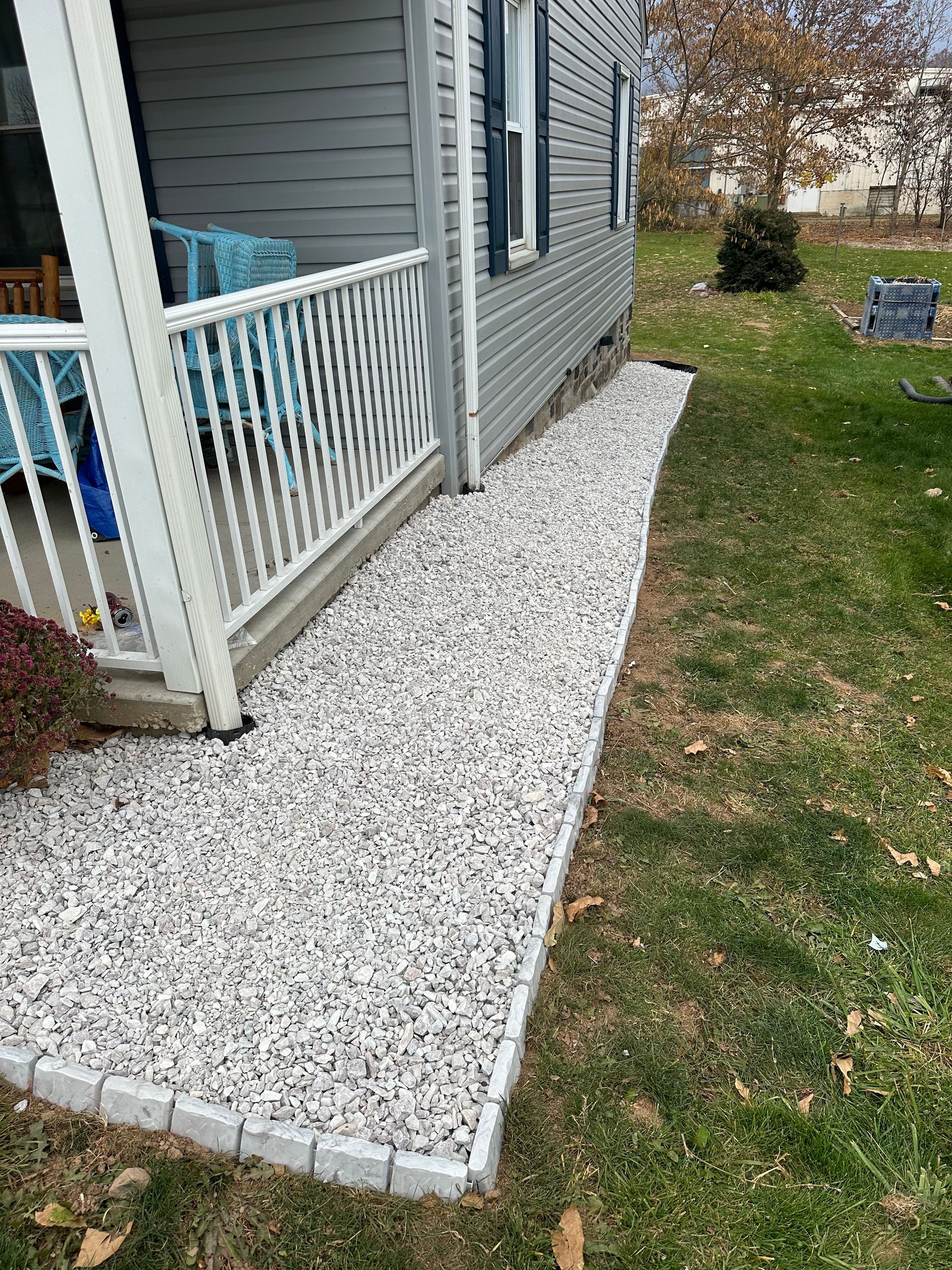 Gray house porch with white railing and a white gravel walkway beside a grassy yard.