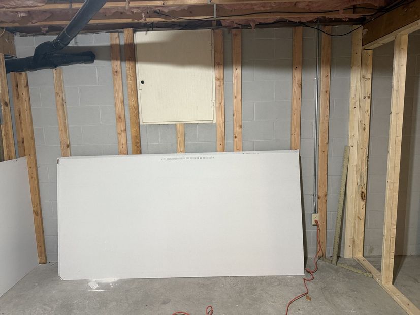 Unfinished basement wall with exposed studs, insulation, and a white board leaning against the concrete floor.