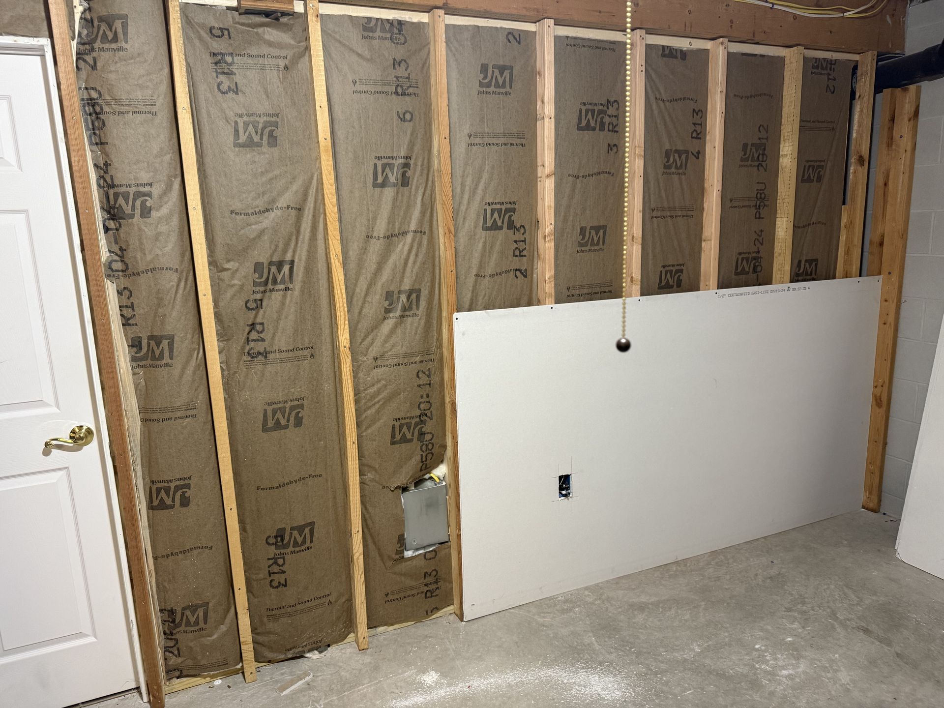 Partially finished basement wall with insulation, exposed studs, and a white board leaning against it