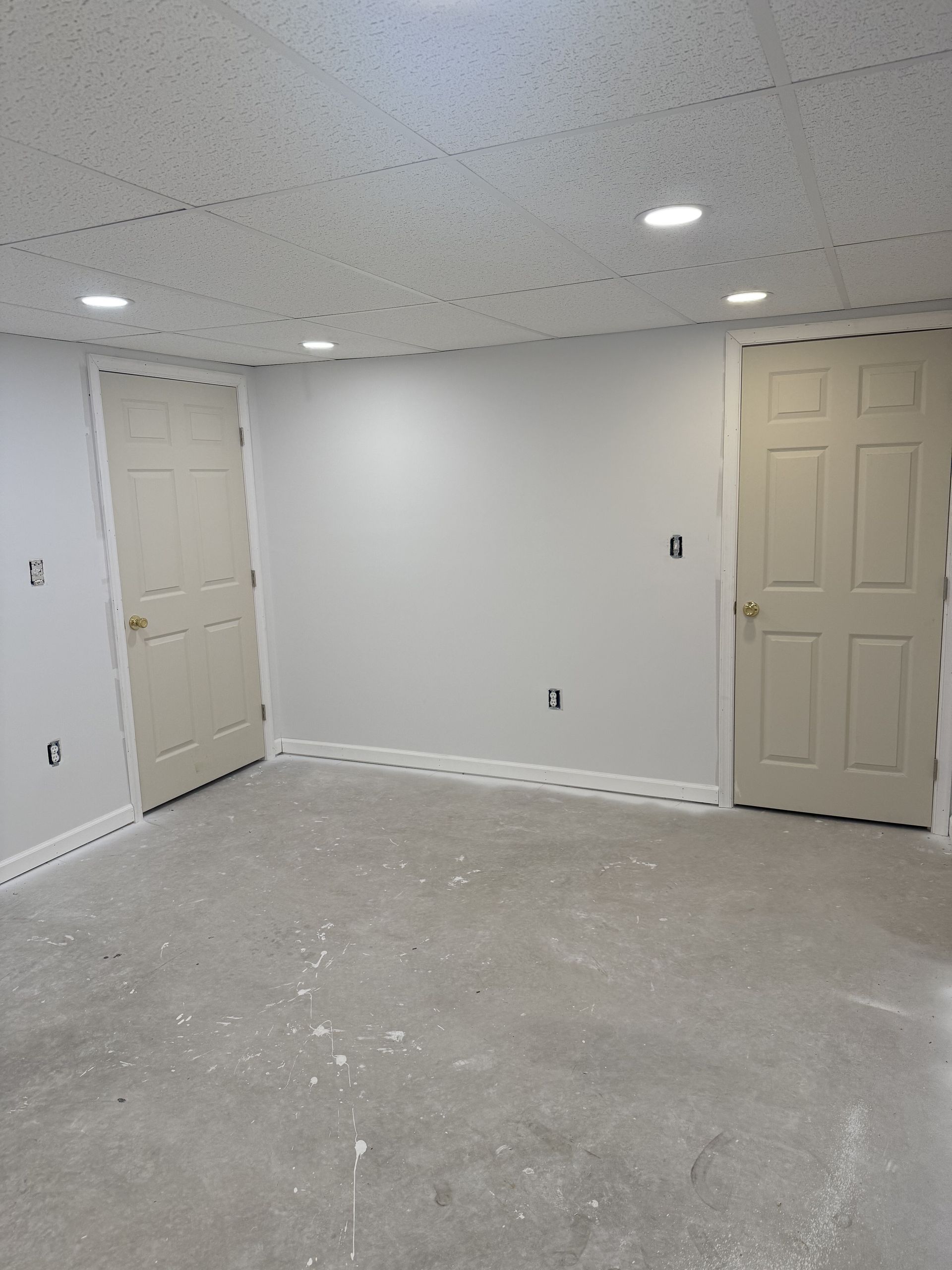Empty unfinished room with gray walls, beige doors, and bare concrete floor under recessed ceiling lights