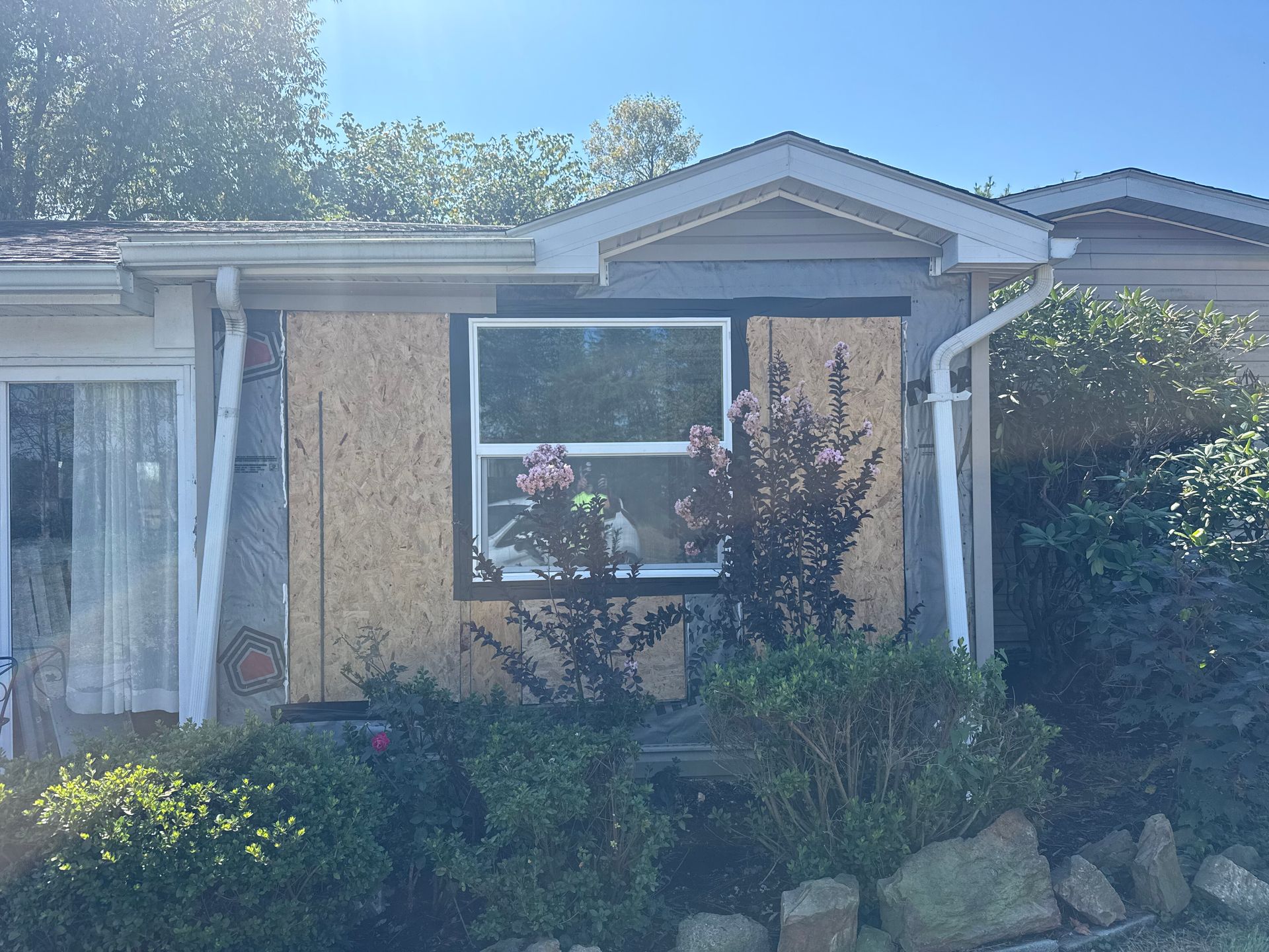 Small beige house with a large front window, porch columns, and overgrown shrubs in front.