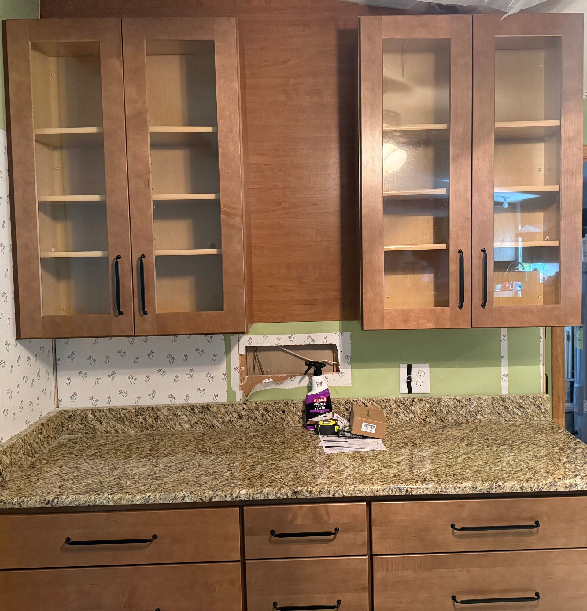 Kitchen with wood cabinets, granite countertop, and a green backsplash under natural light.