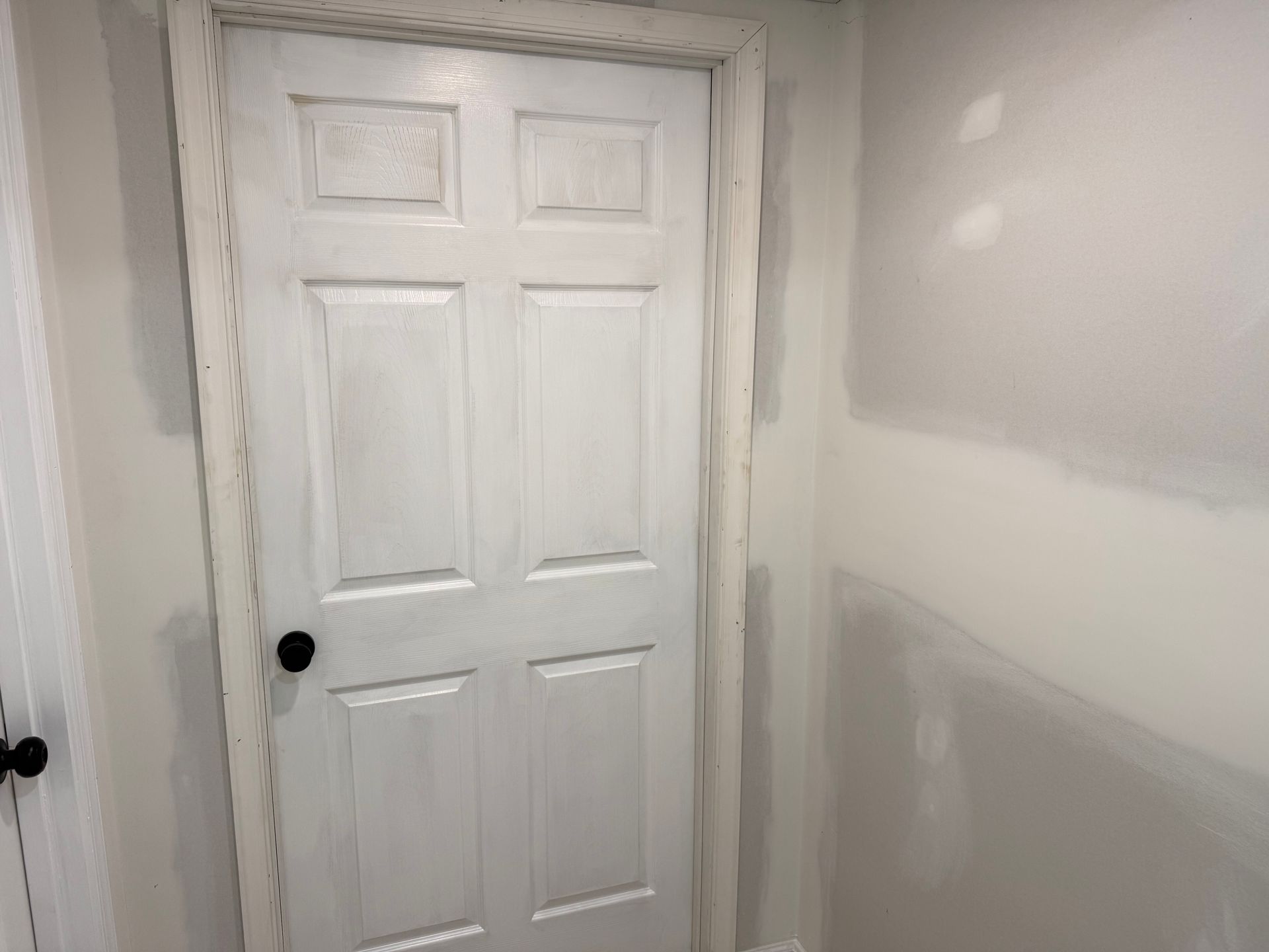 White paneled door in a newly painted room with unfinished drywall patches.