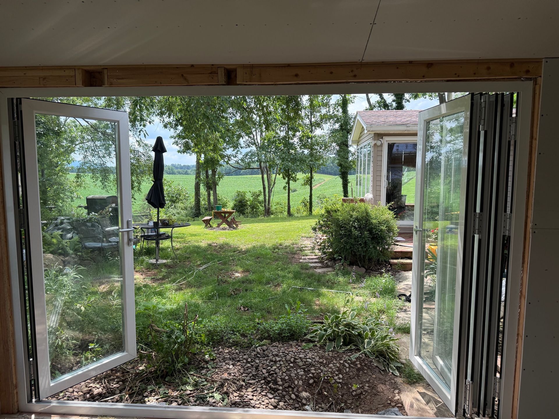 Open French doors leading to a grassy backyard with trees, patio furniture, and a small shed.
