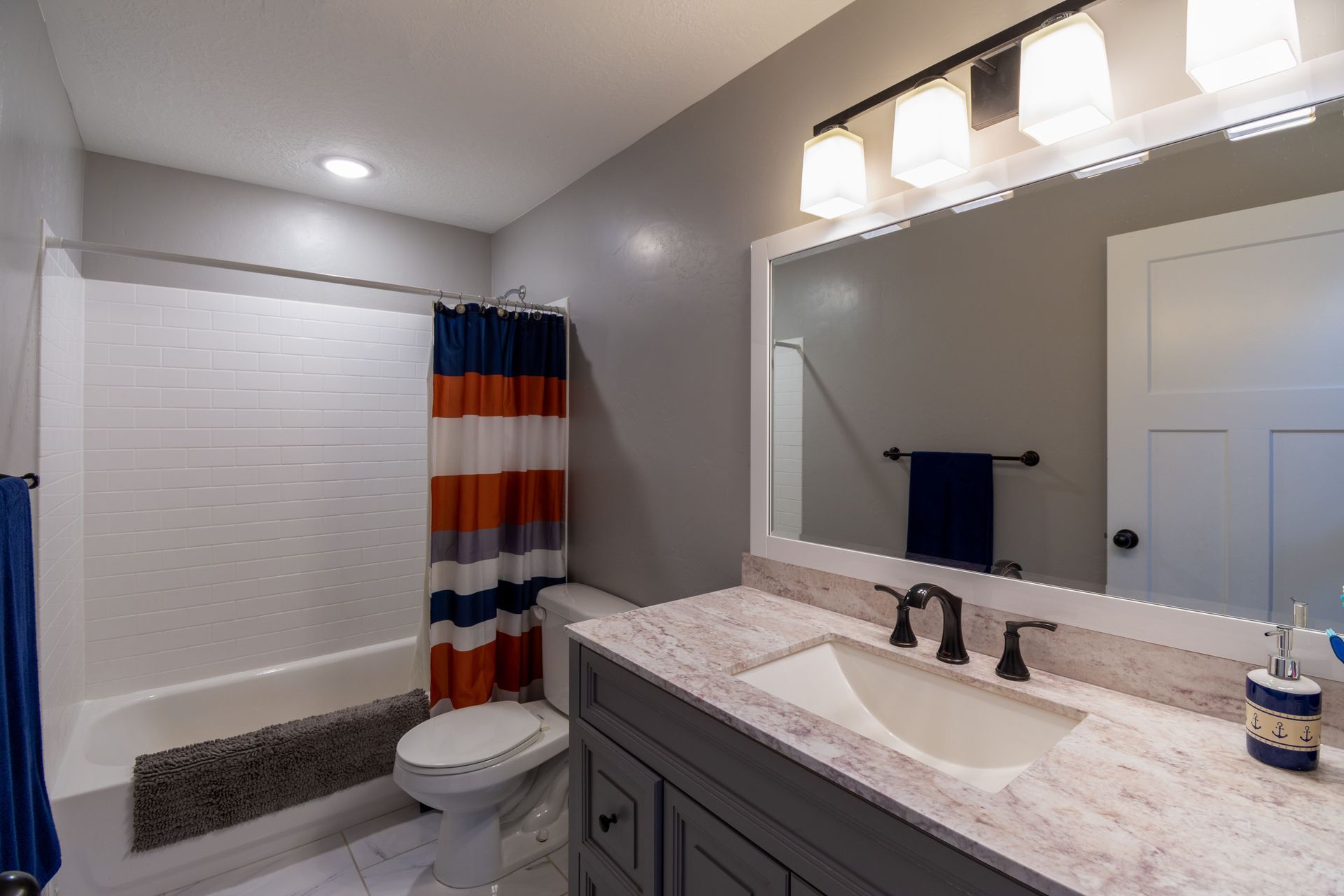 Bathroom with double vanity, large mirror, toilet, and striped shower curtain in a gray-and-white room