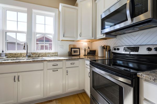 Bright white kitchen with granite countertops, stainless steel stove, microwave, and double windows above the sink